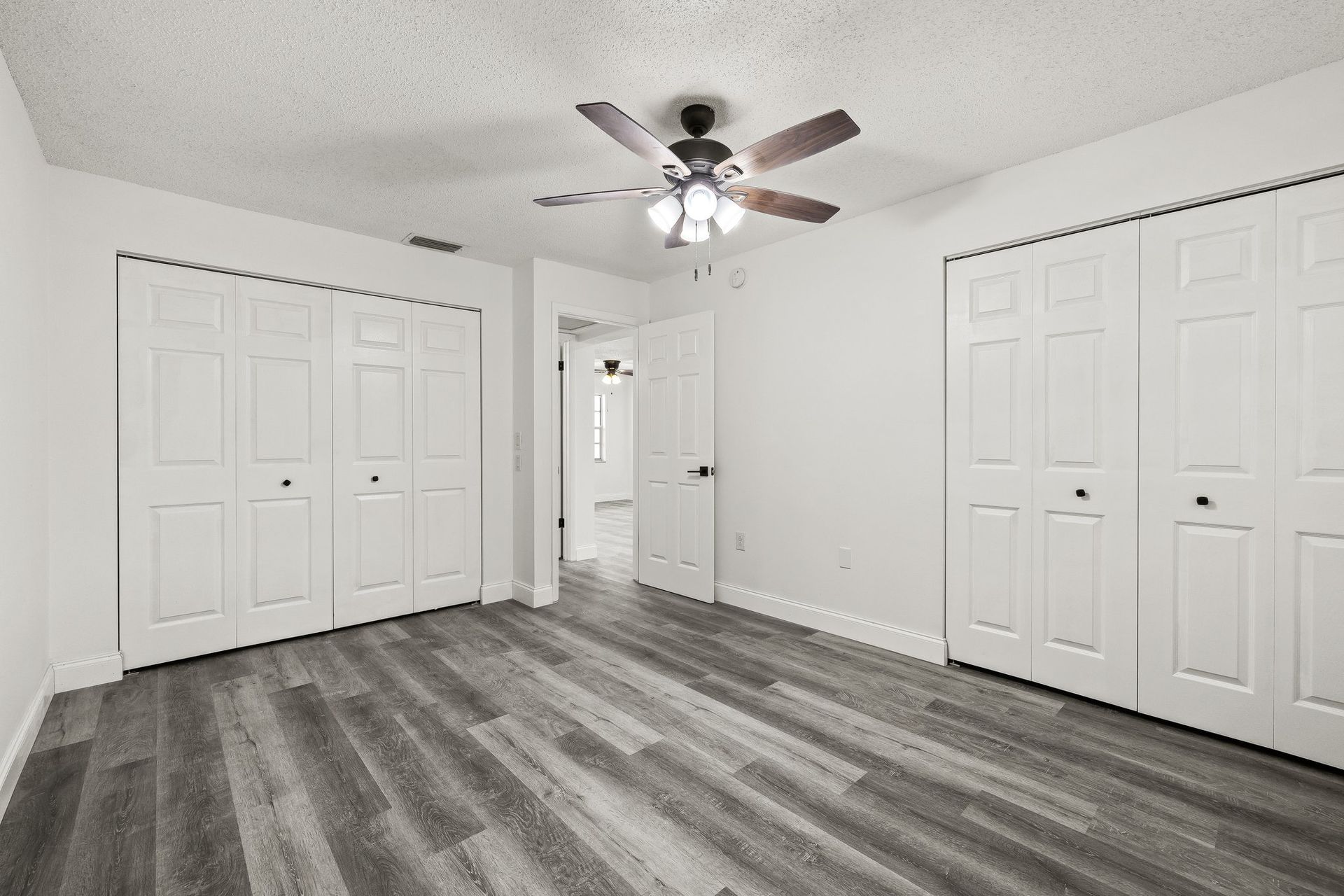 Empty white bedroom with gray wood floors, ceiling fan, and double closet doors