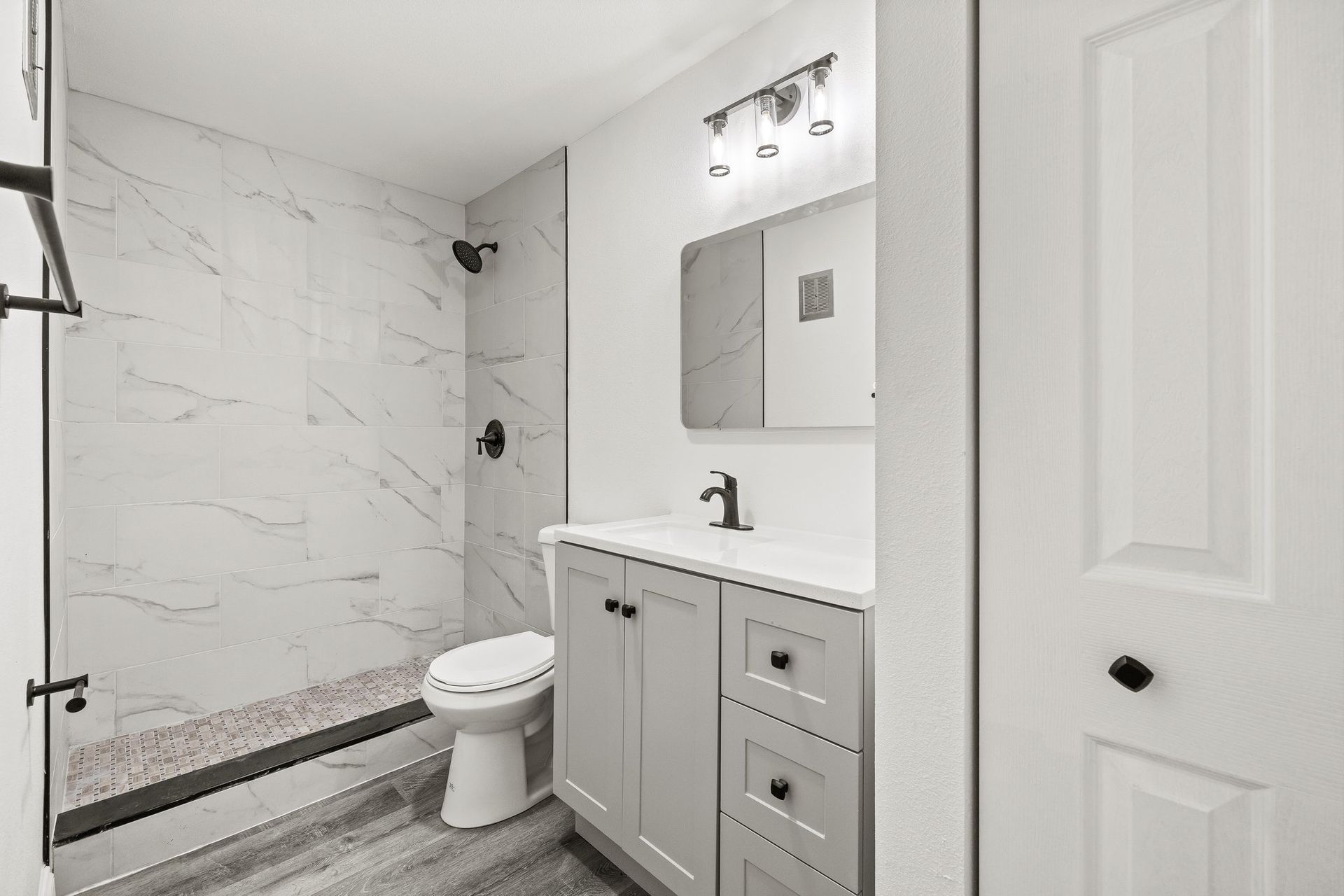 Walk-in shower with marble-look tile, matte black fixtures, and hexagon mosaic tile shower floor