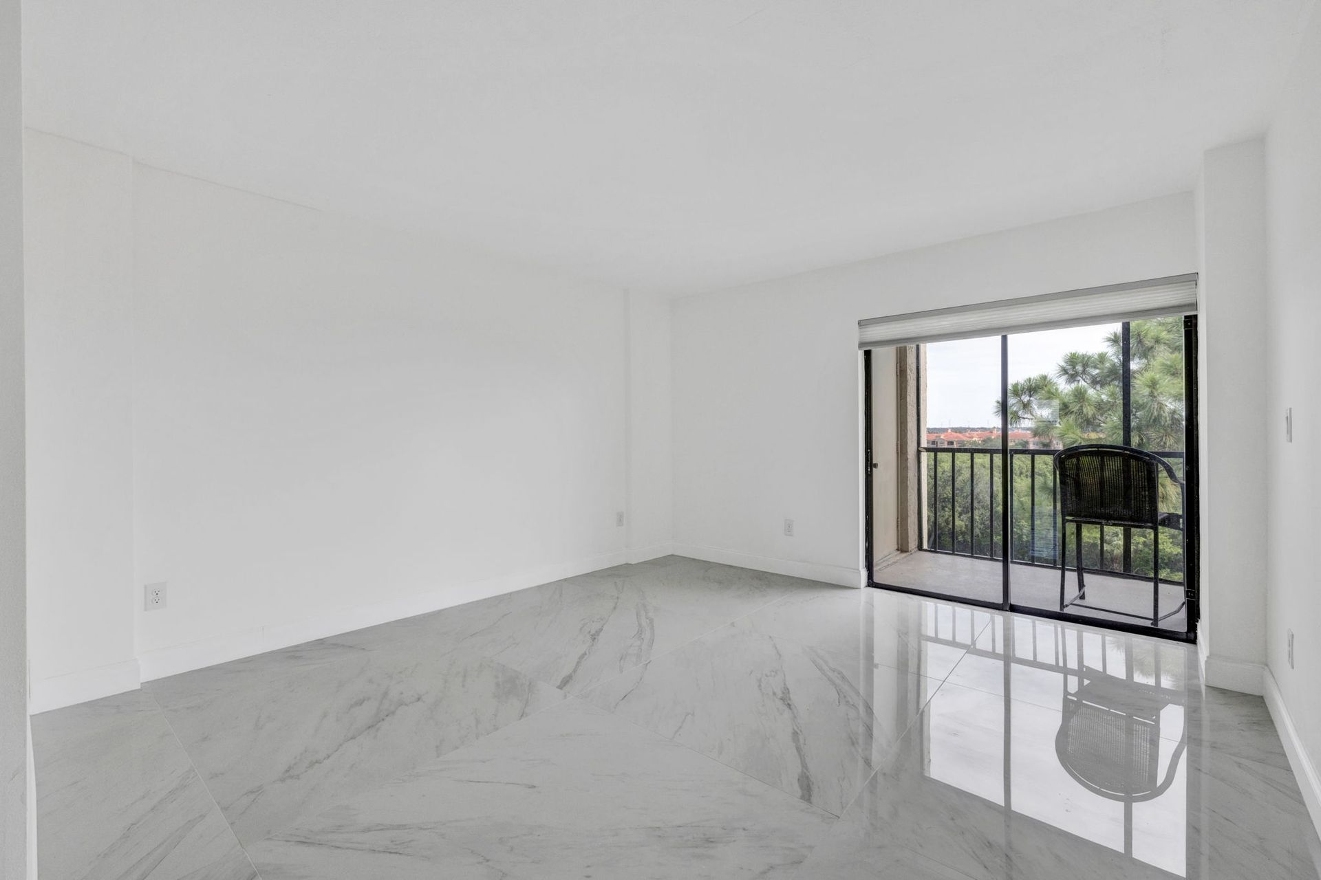 Empty white room with glossy tile floor and sliding glass door to a balcony.