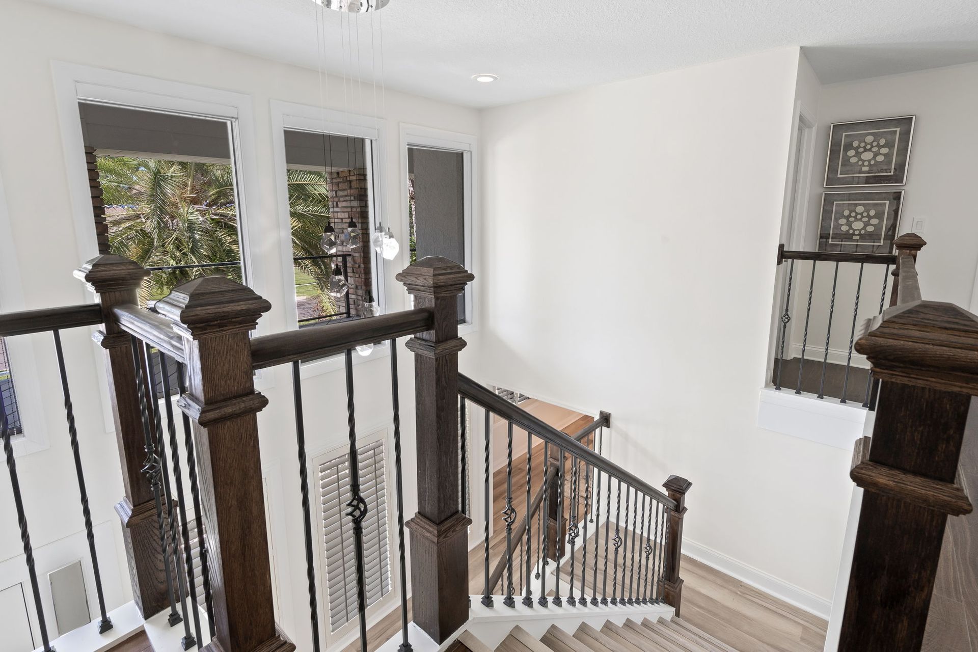 Staircase landing with dark wood railing, white walls, and windows overlooking trees