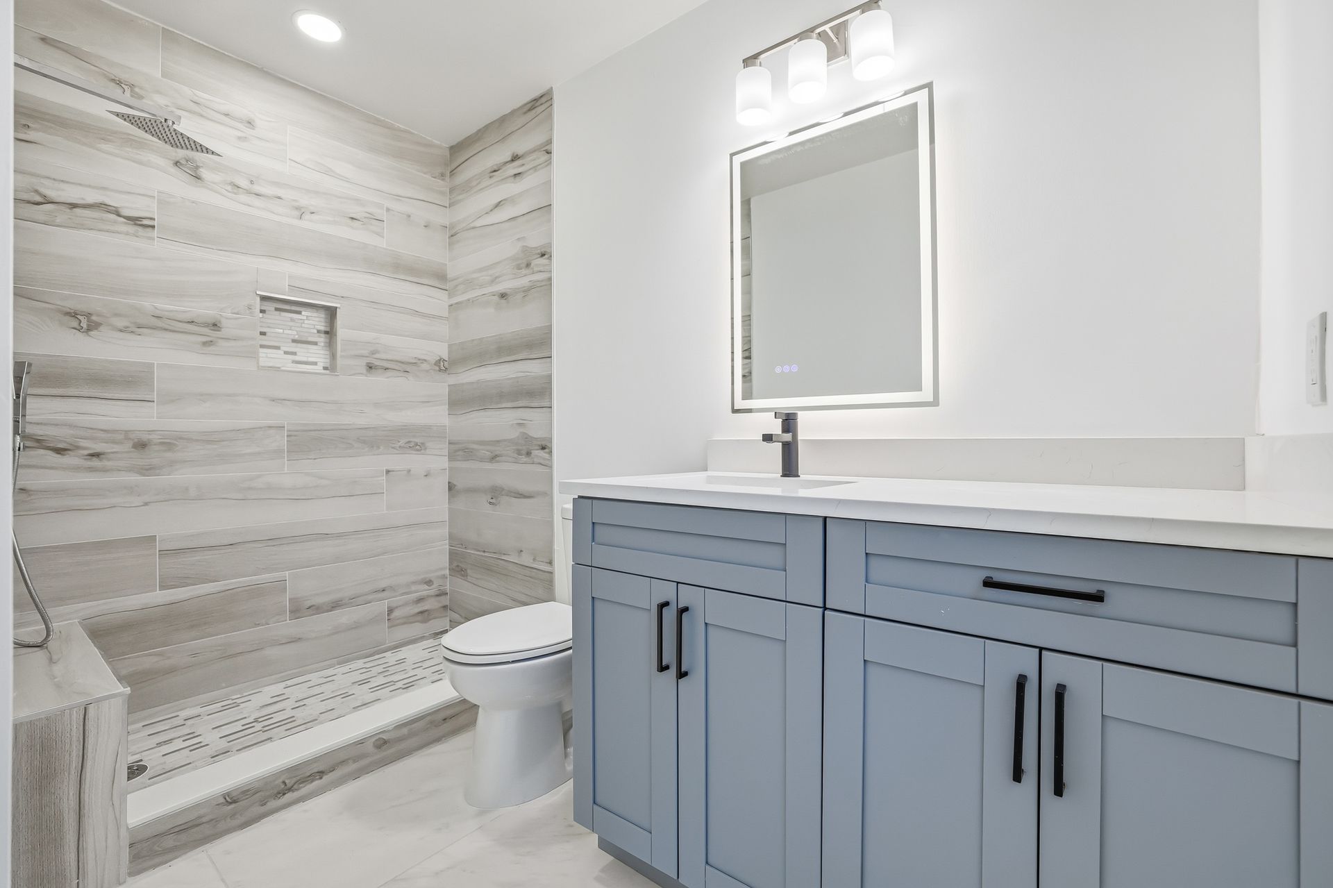 Modern white bathroom with gray vanity, mirror, toilet, and tiled shower.