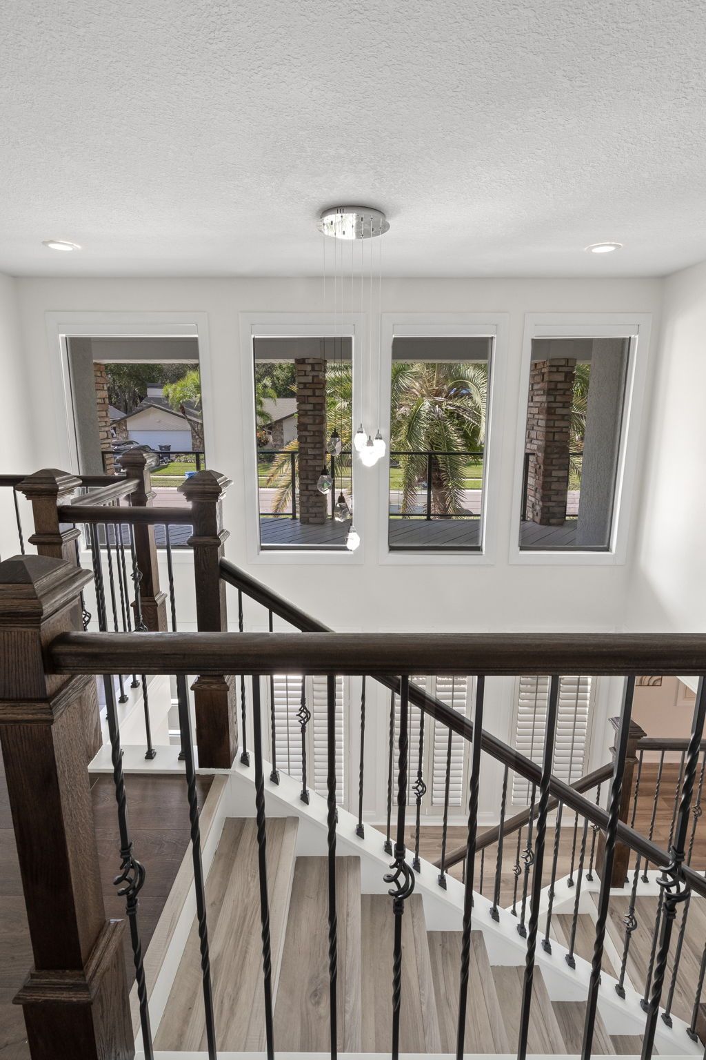 Upper landing with wooden railing and staircase beside four tall windows overlooking trees outdoors