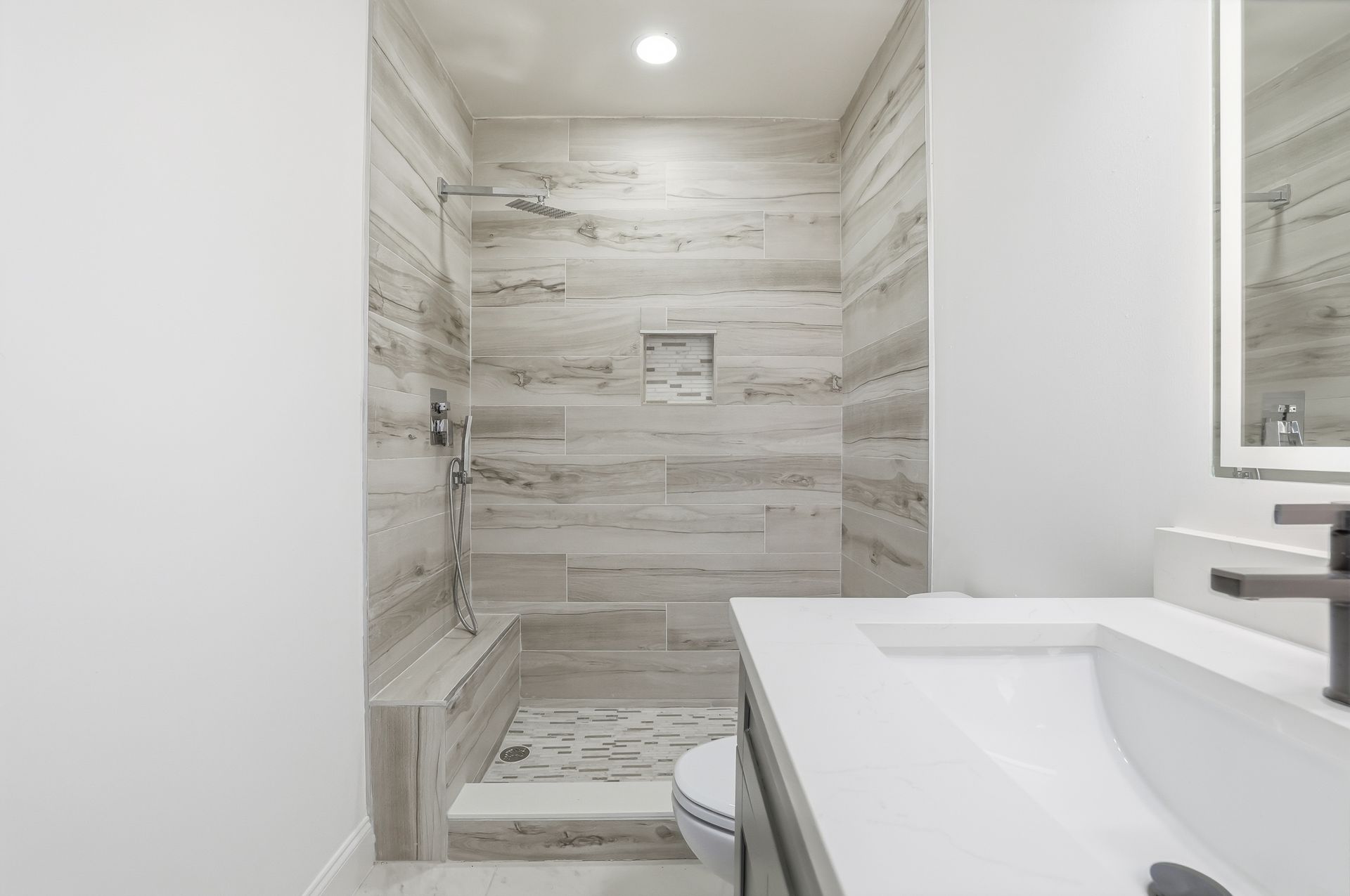 Modern walk-in shower with light wood-look tile, rainfall showerhead, and white vanity in a bright bathroom