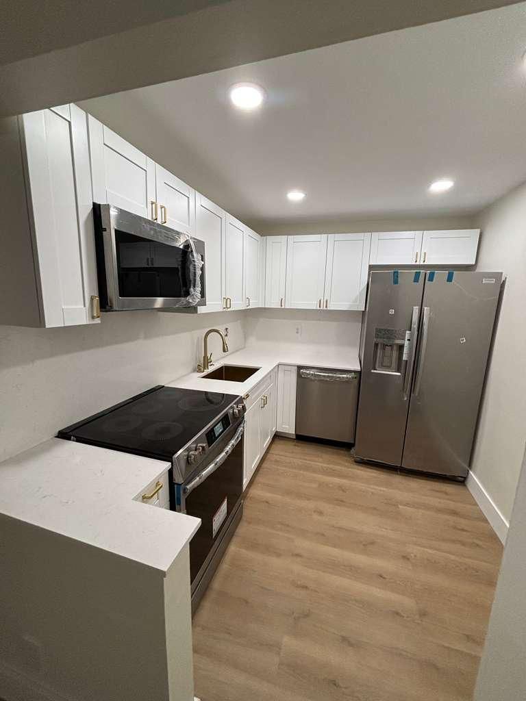 Modern white kitchen with stainless steel appliances, wood floor, and recessed lighting.