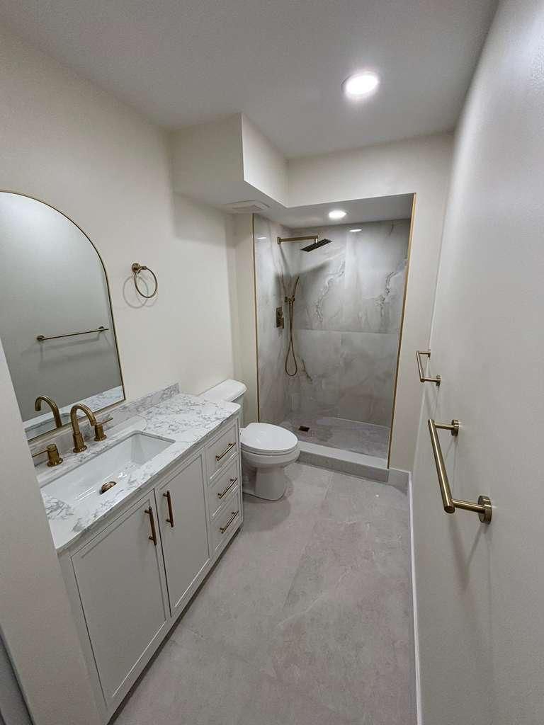 Bright modern bathroom with white vanity, mirror, toilet, and walk-in shower.