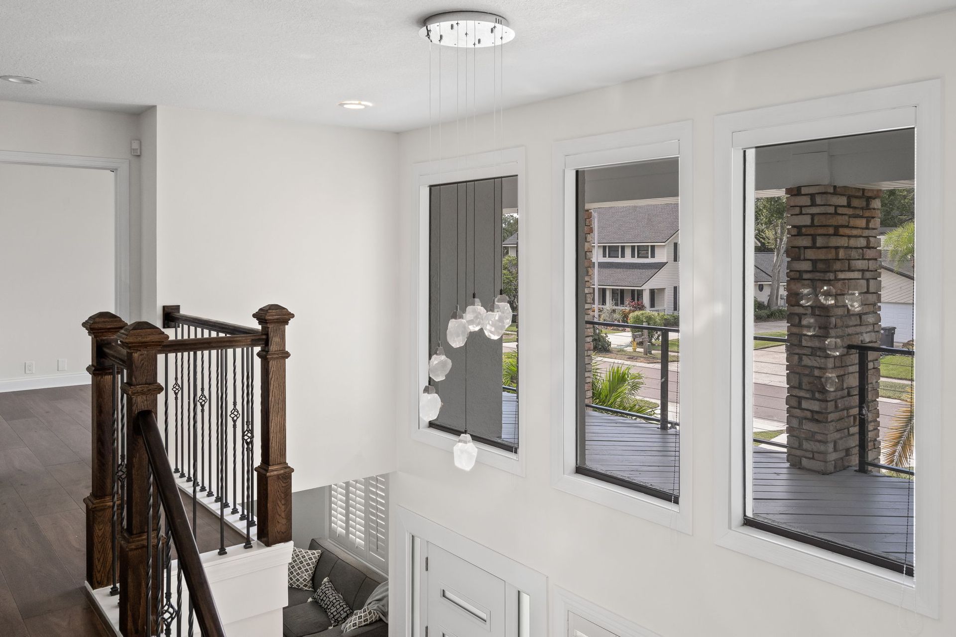 Bright foyer with staircase railing and three windows overlooking a front porch and stone column