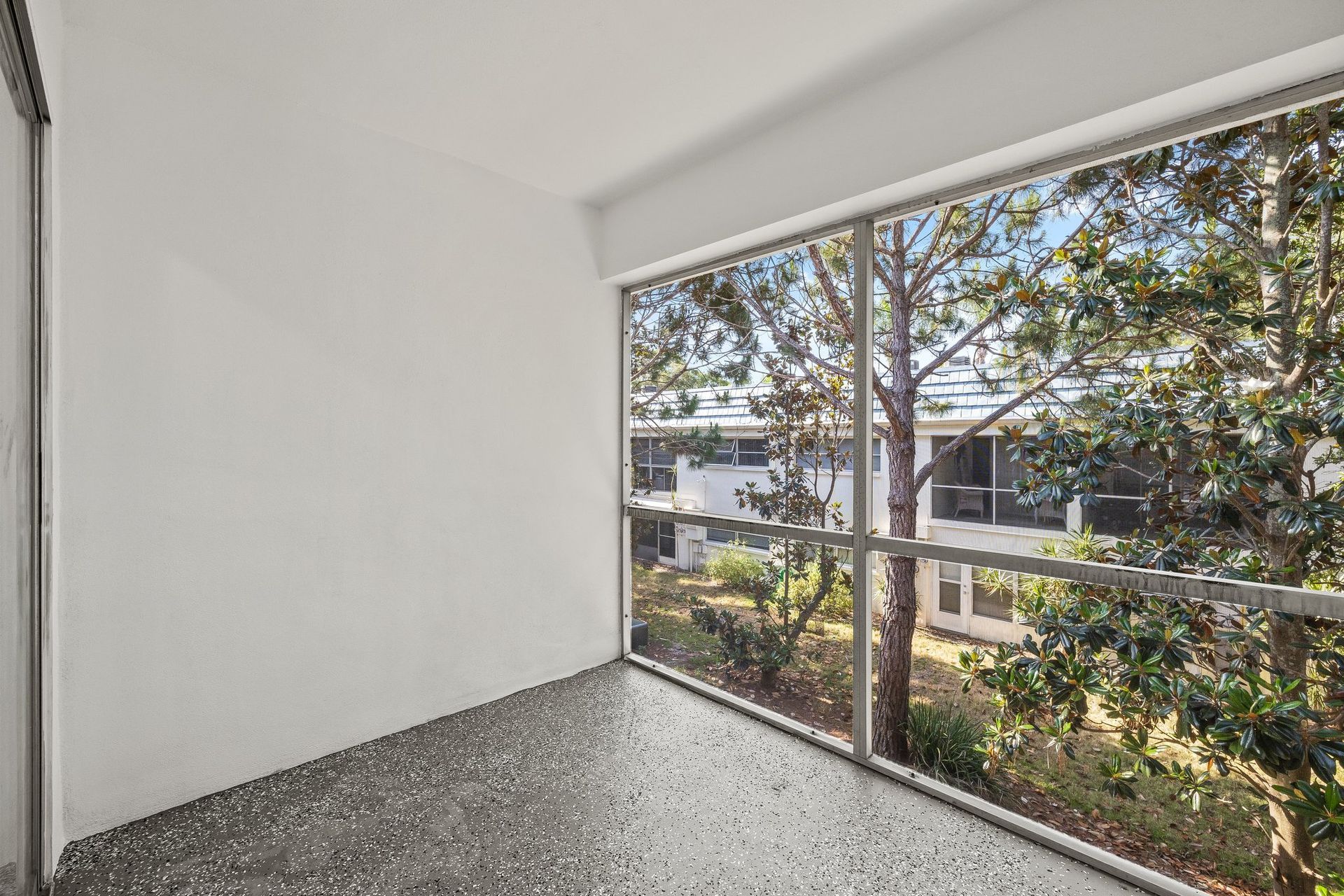 Empty white room with speckled floor and large window overlooking trees and nearby buildings