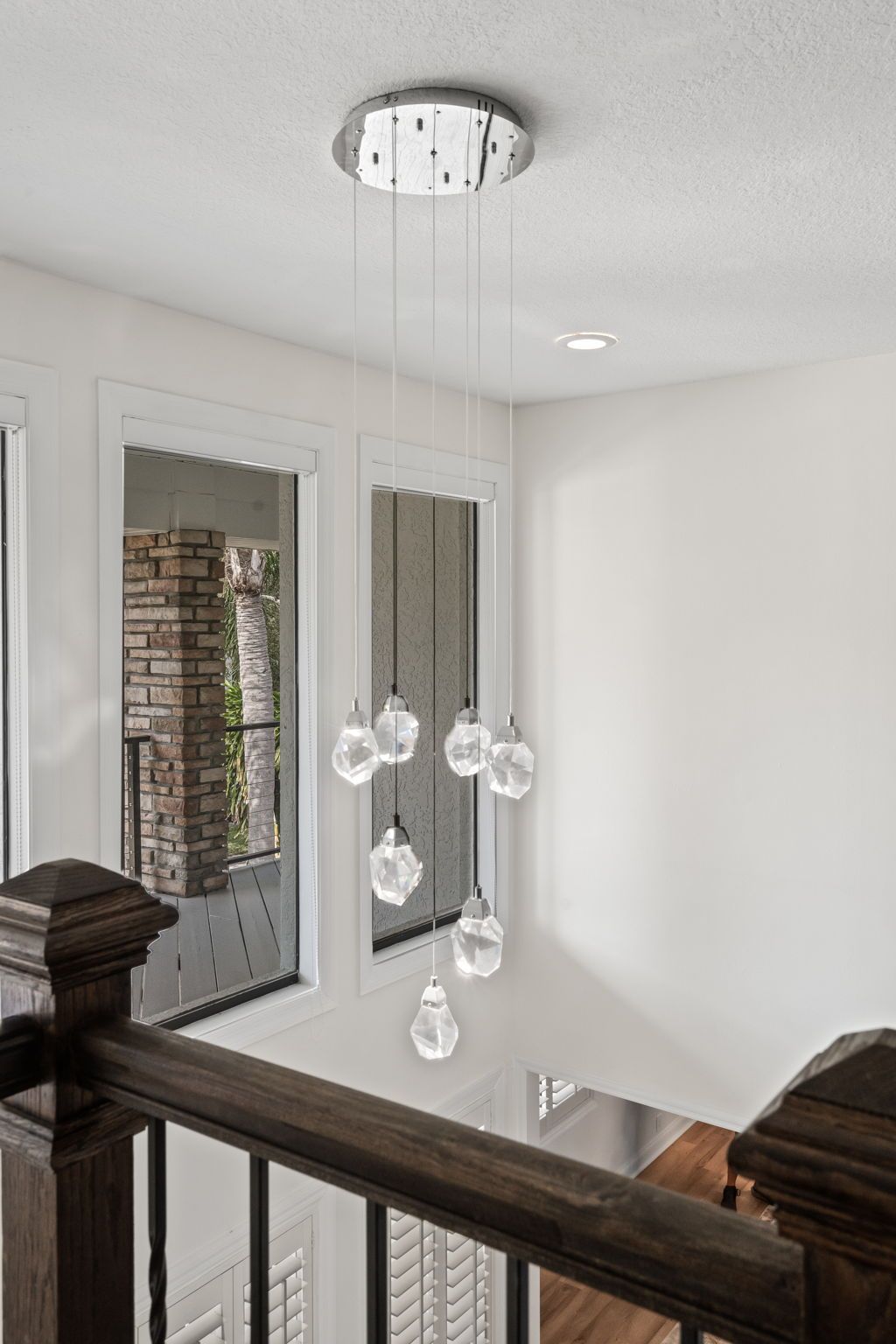 Modern stair landing with hanging glass pendant lights and white walls near a window.