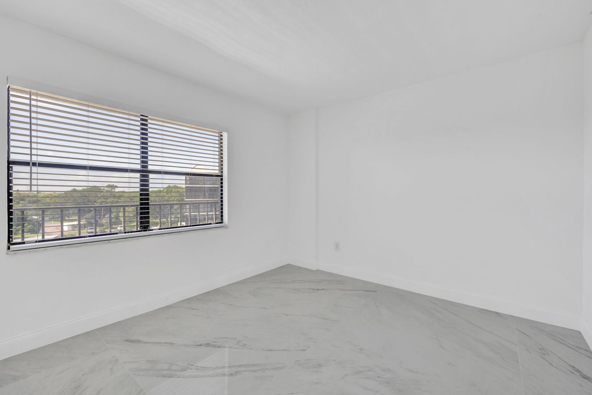 Empty white room with gray tile floor and a large window with blinds.
