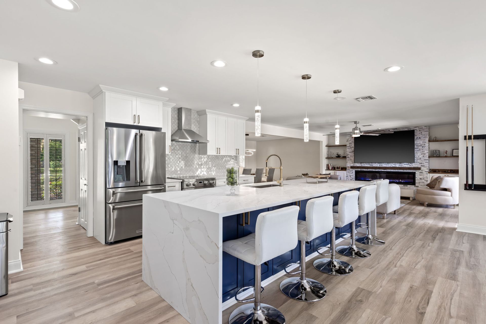 Modern white kitchen with island, blue barstools, stainless steel appliances, and open living area