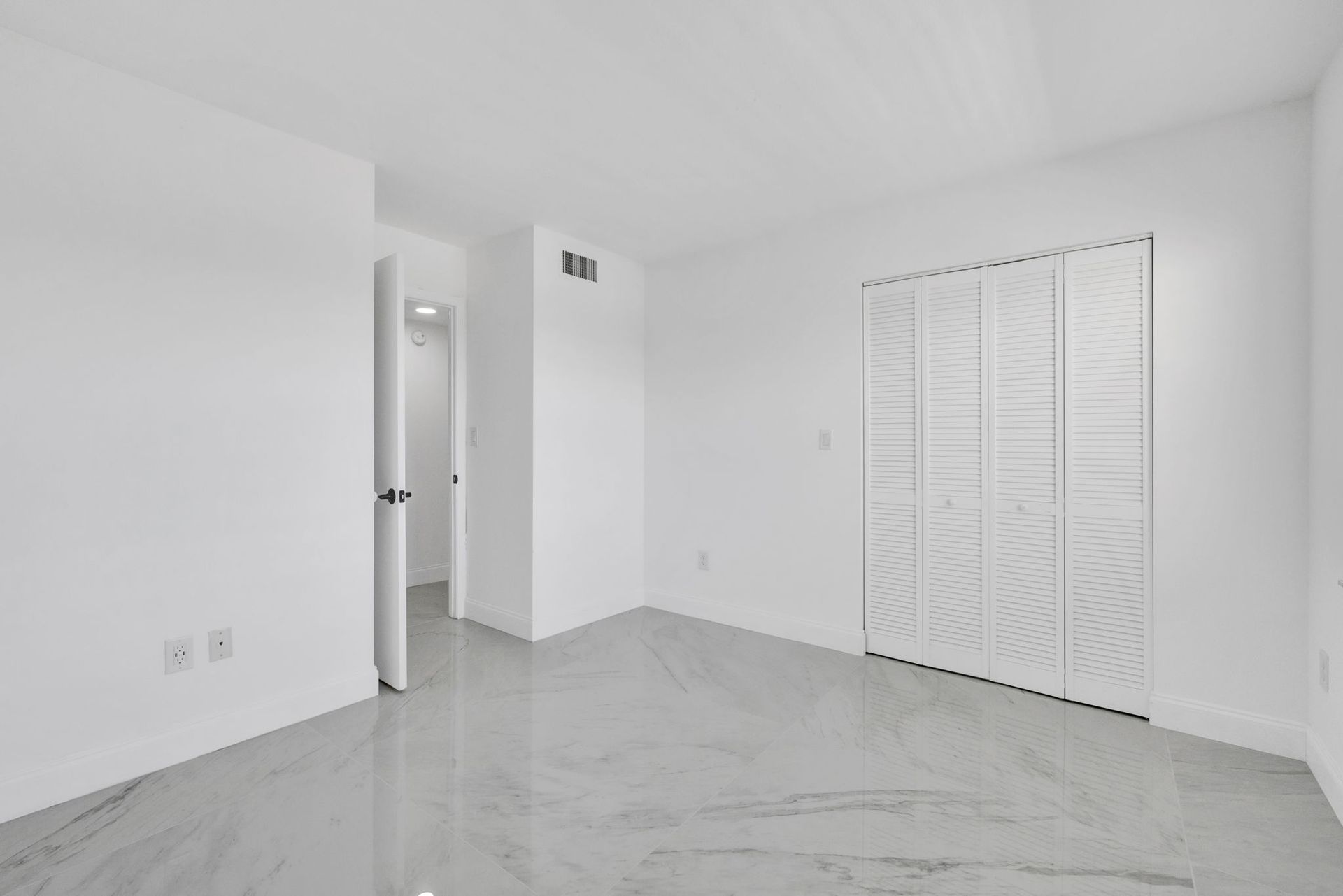 Empty white bedroom with marble tile floor, closet doors, and an open doorway