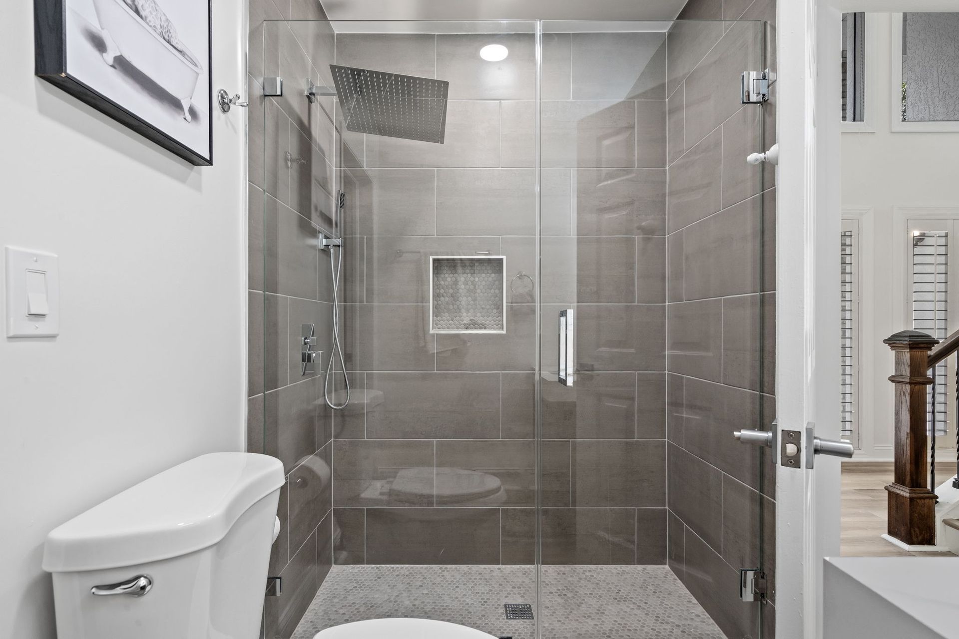 Glass walk-in shower with gray tile, built-in niche, and white bathroom fixtures.