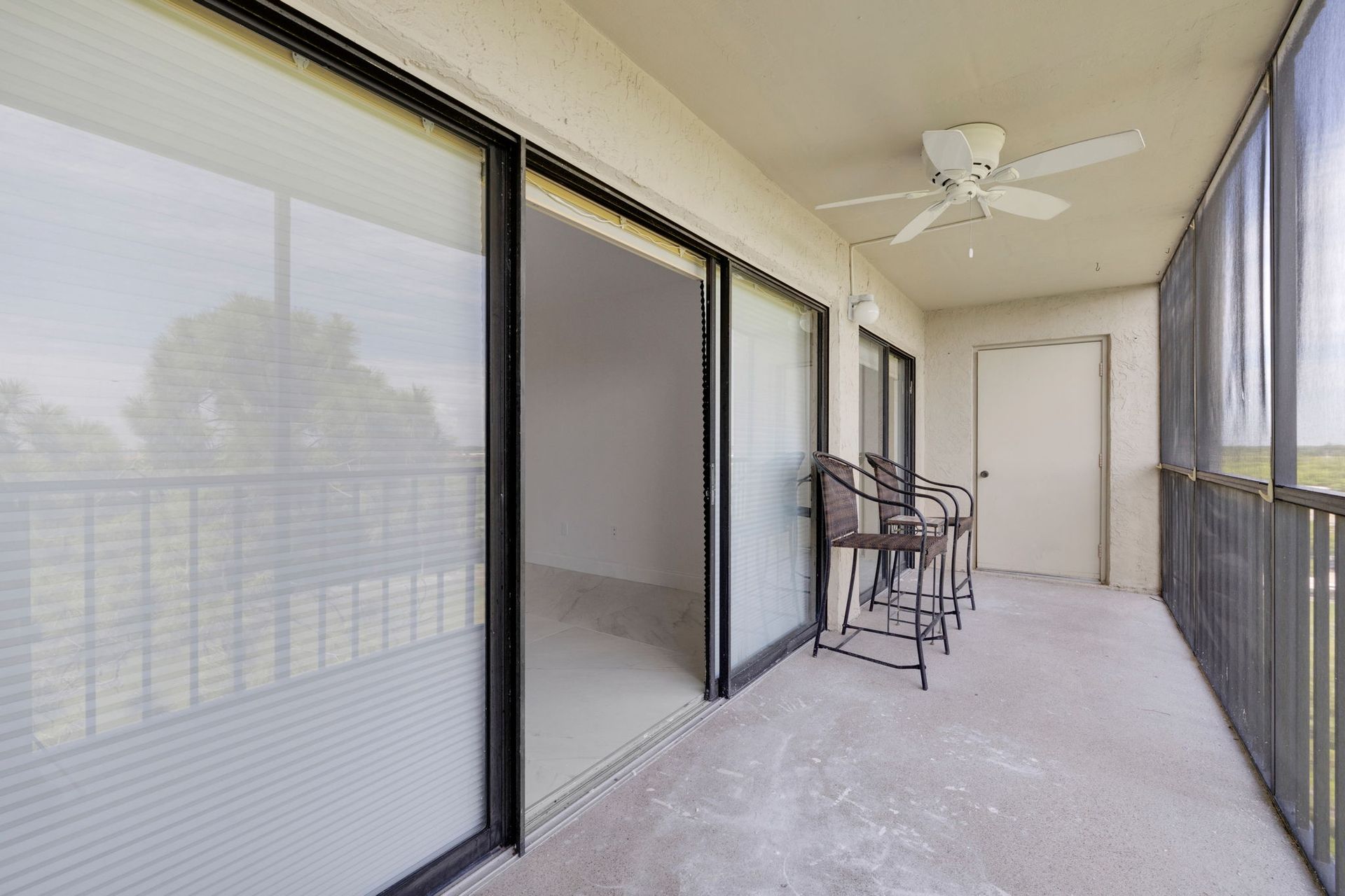 Screened balcony with sliding glass doors, patio chairs, and a ceiling fan.