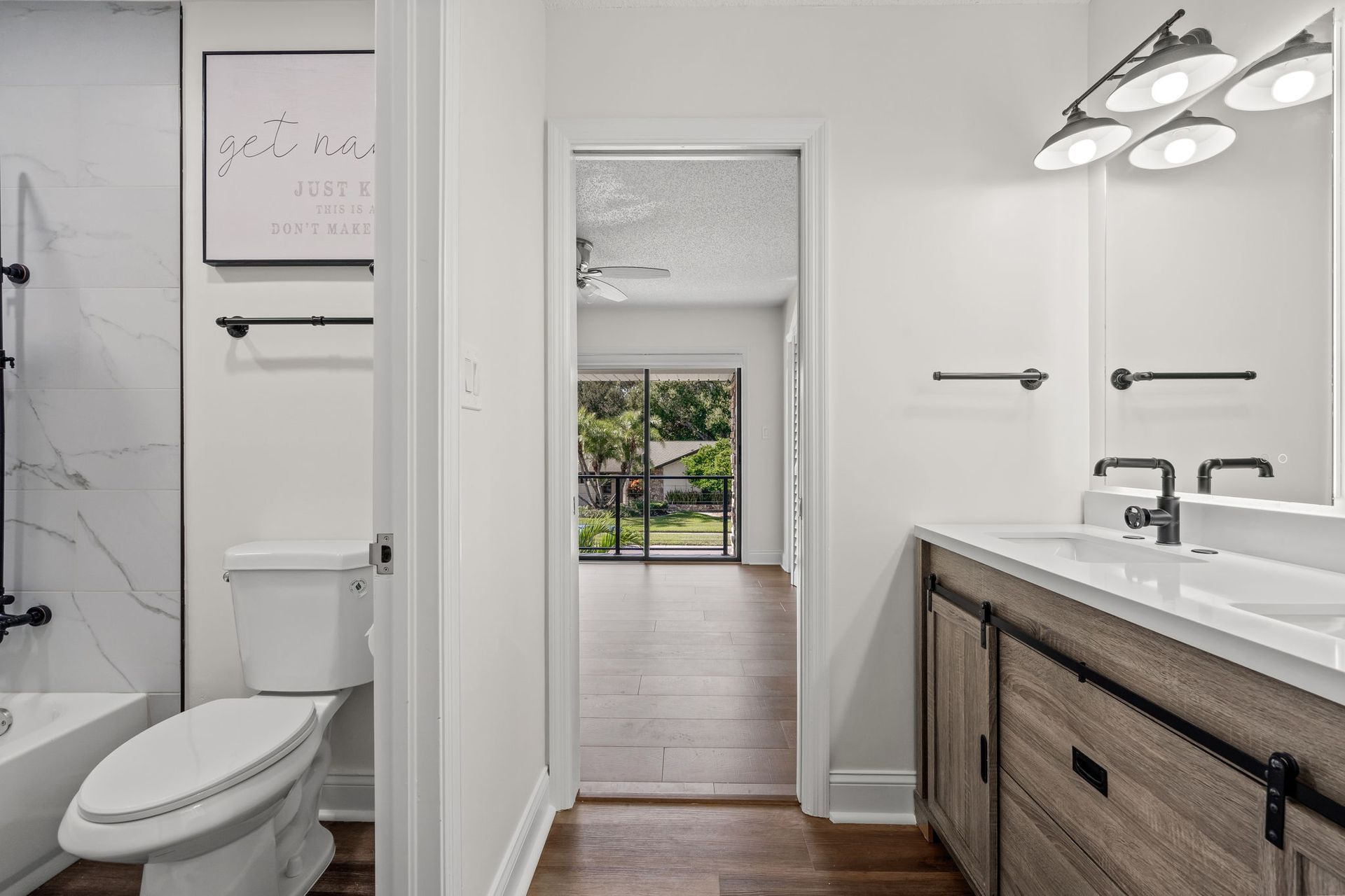 Bright modern bathroom with toilet, vanity, and doorway to a bedroom with sliding glass doors.