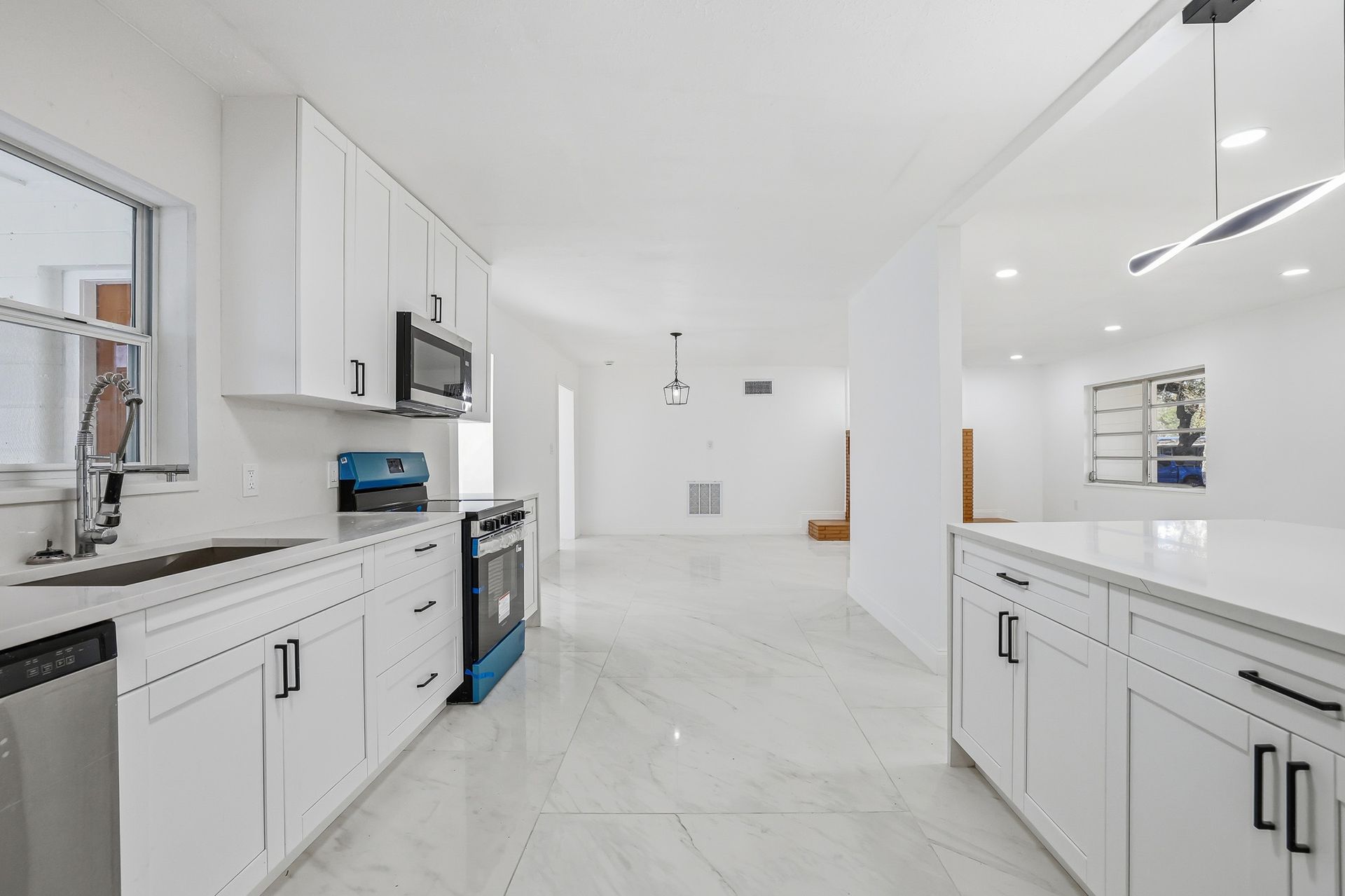 Bright modern white kitchen with island, stainless appliances, and large windows