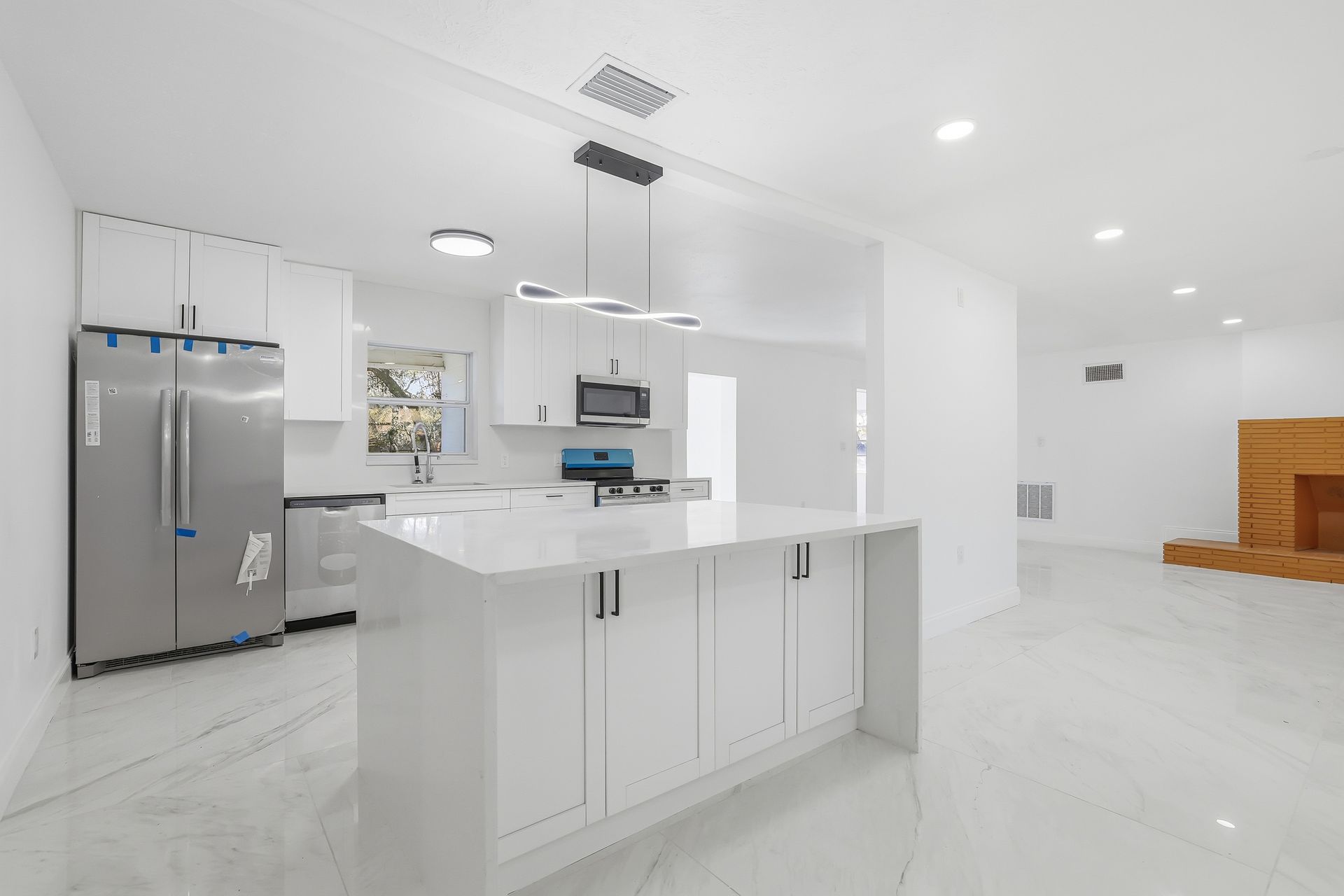 Bright modern kitchen with white cabinets, island, stainless fridge, and open living area with wood stairs