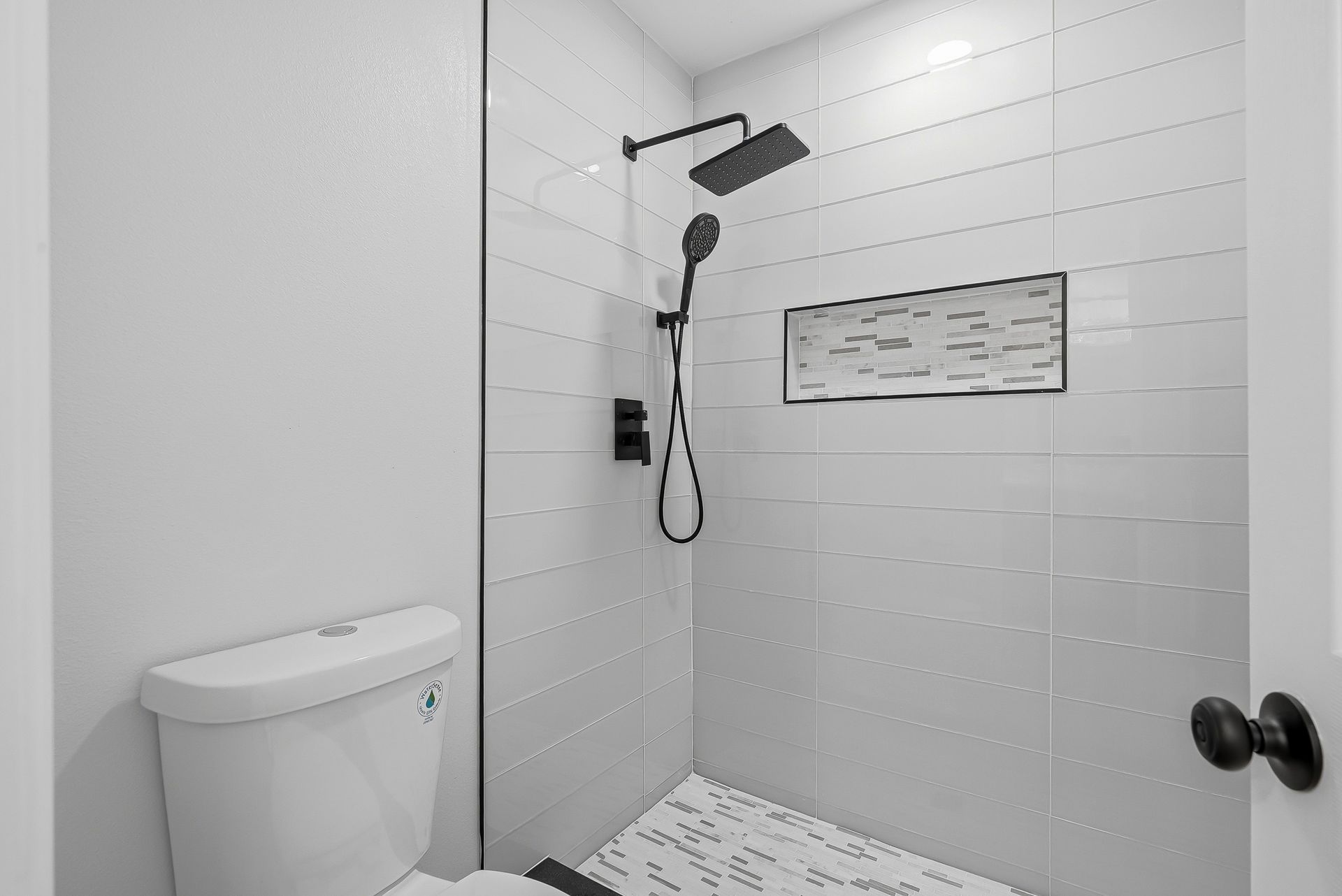 Minimalist walk-in shower with white plank tile, matte black rainfall shower head, and mosaic accent niche