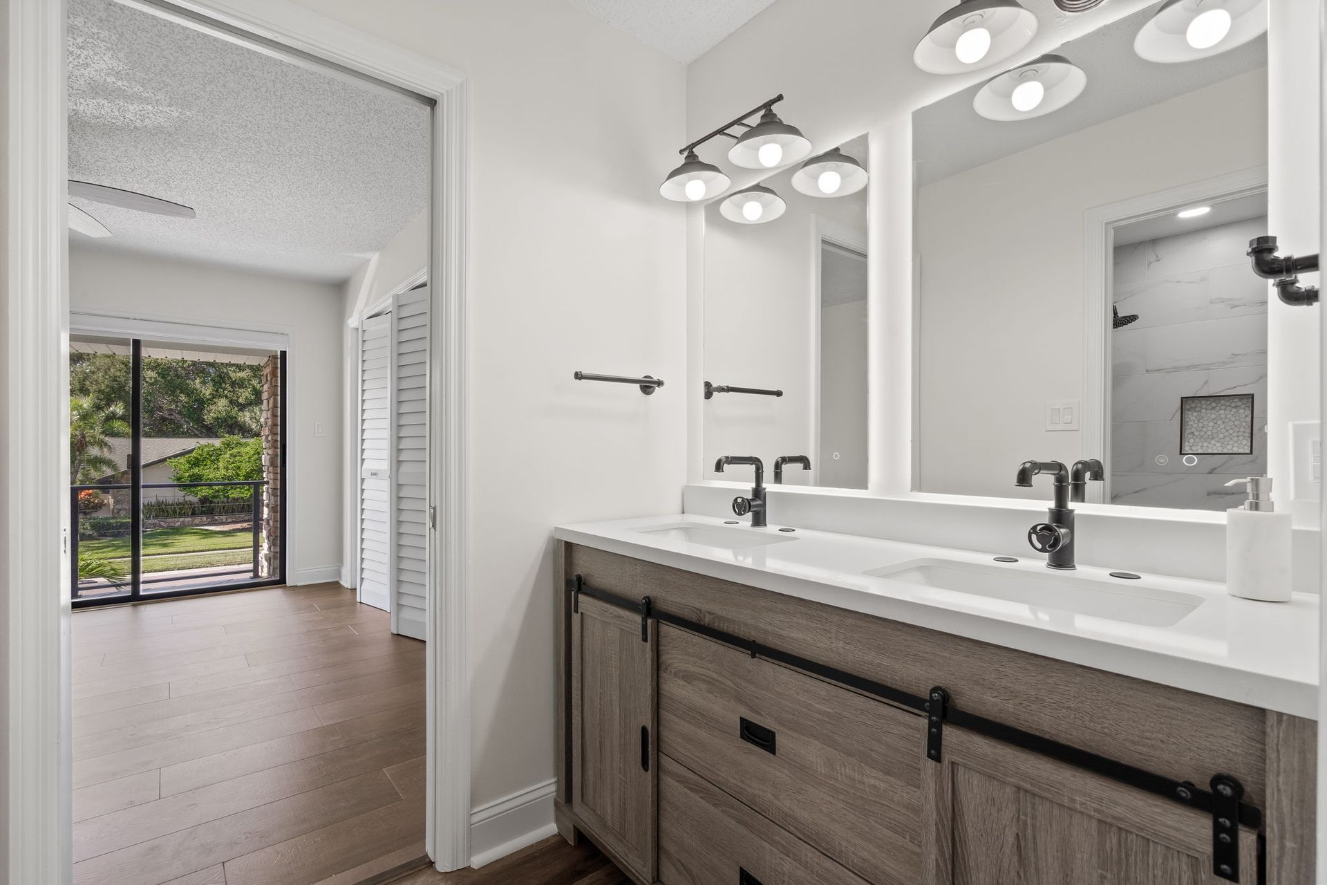 Bright bathroom vanity with dual mirrors and lights, opening to a hallway with hardwood floors and garden view.