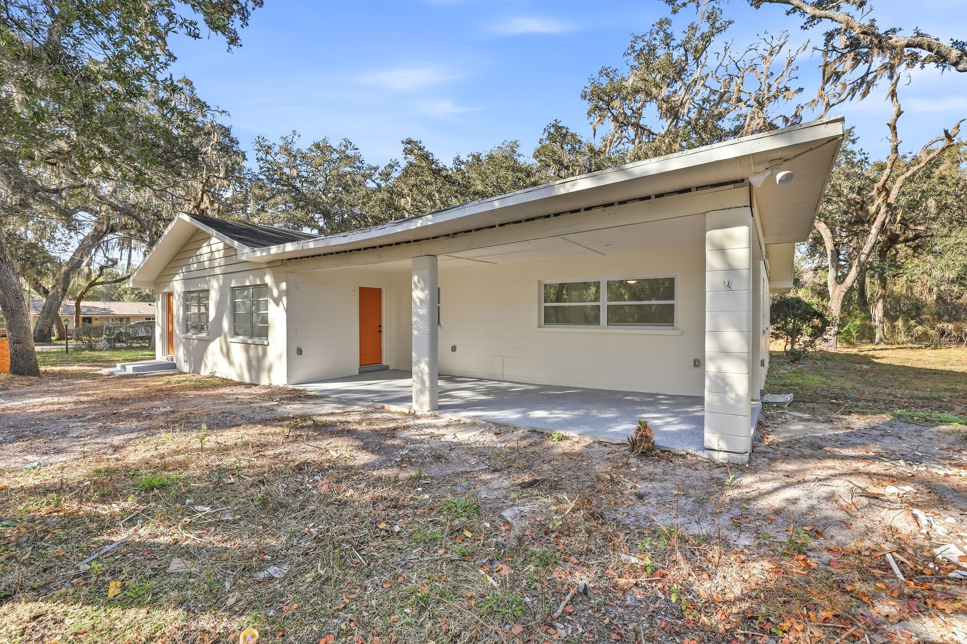 Single-story white house with orange door, front porch, and trees in the yard