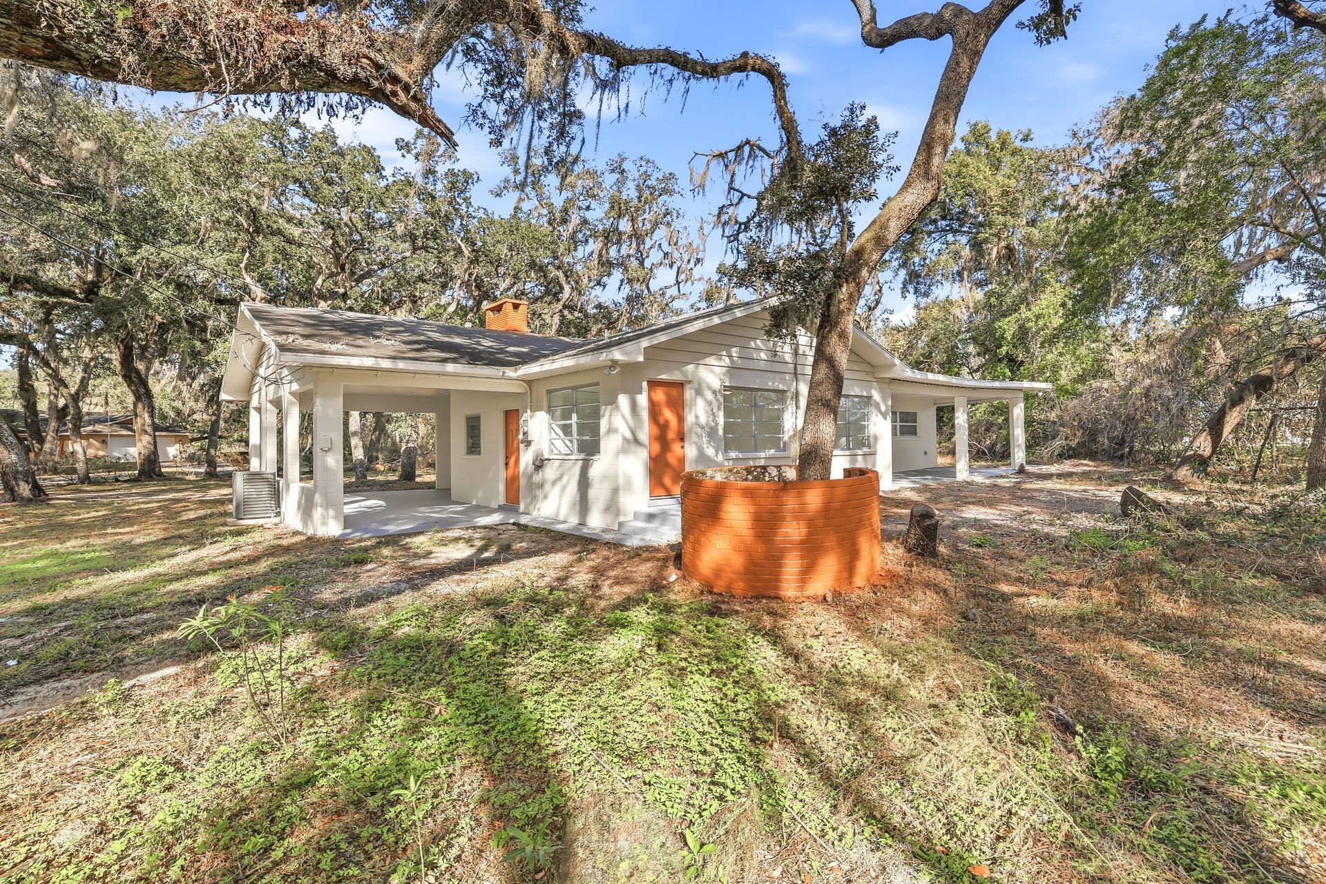 White house with large trees and a bright orange barrier in front, set in a grassy yard.