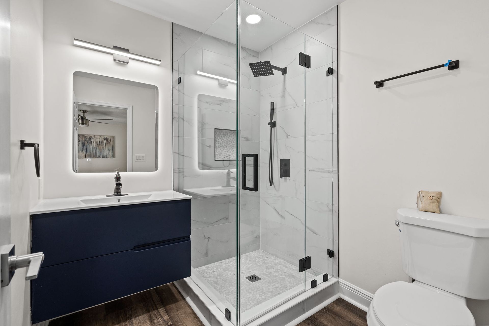 Modern white bathroom with glass shower, navy vanity, and toilet