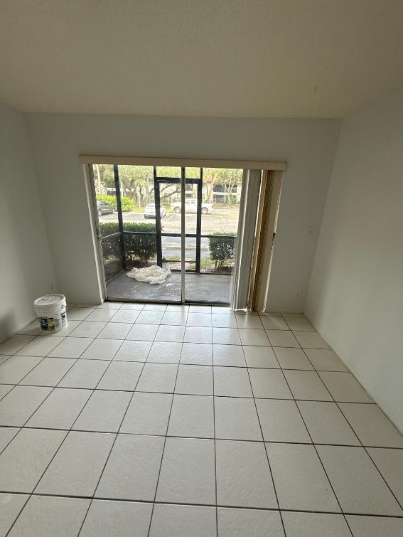 Empty tiled room with sliding glass doors opening to a patio and greenery outside