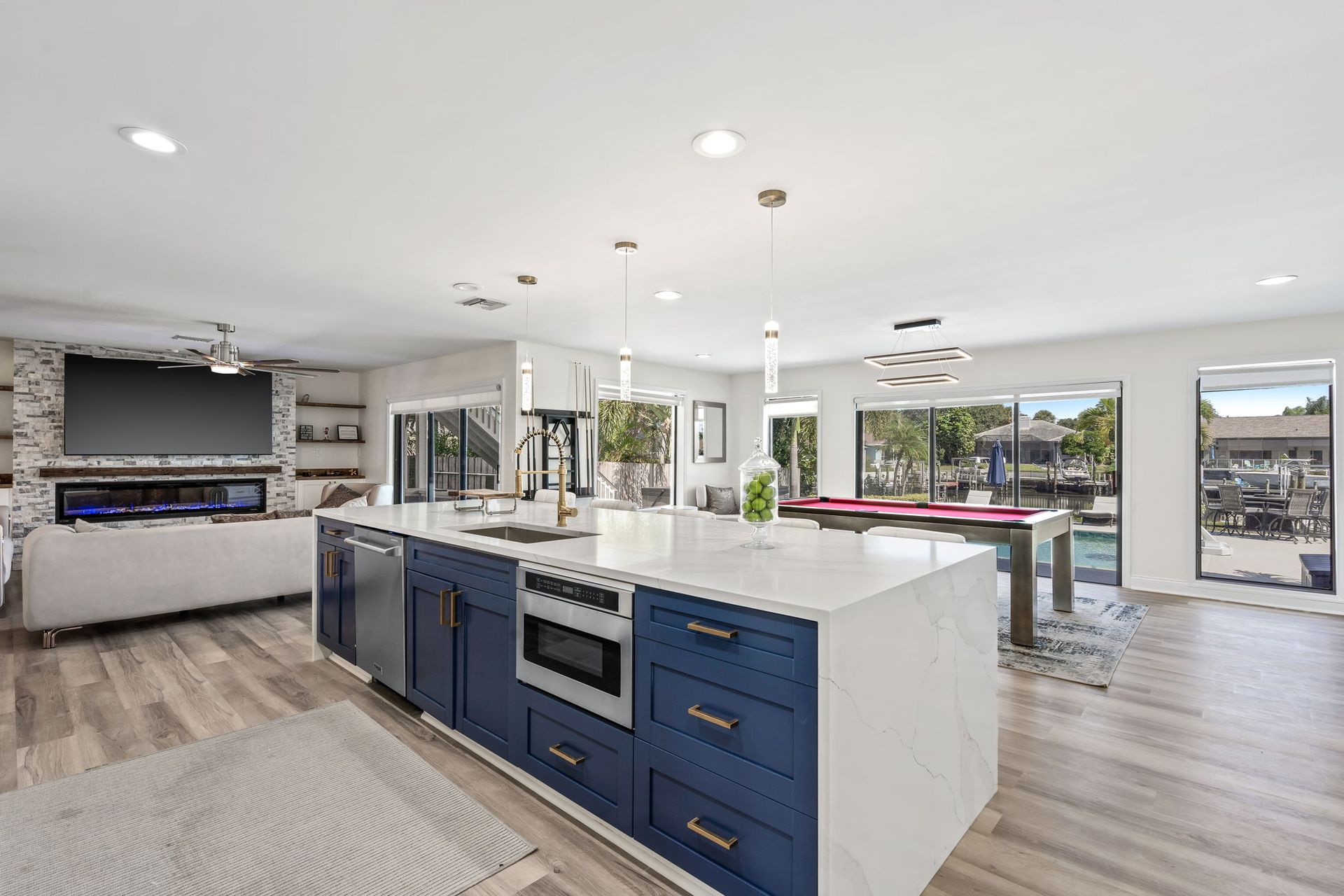 Bright modern kitchen with blue island, white countertops, and large windows overlooking a patio.