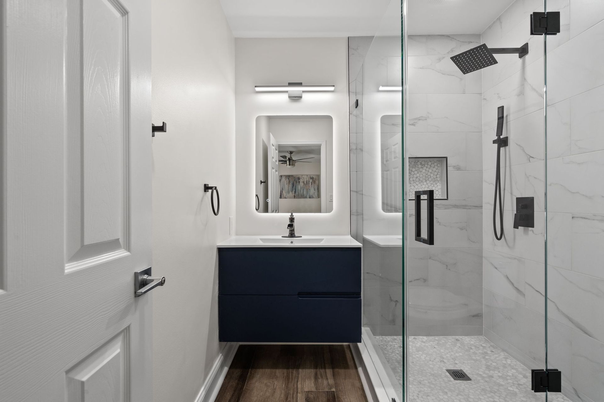 Modern bathroom with white walls, navy vanity, mirror, and glass shower enclosure