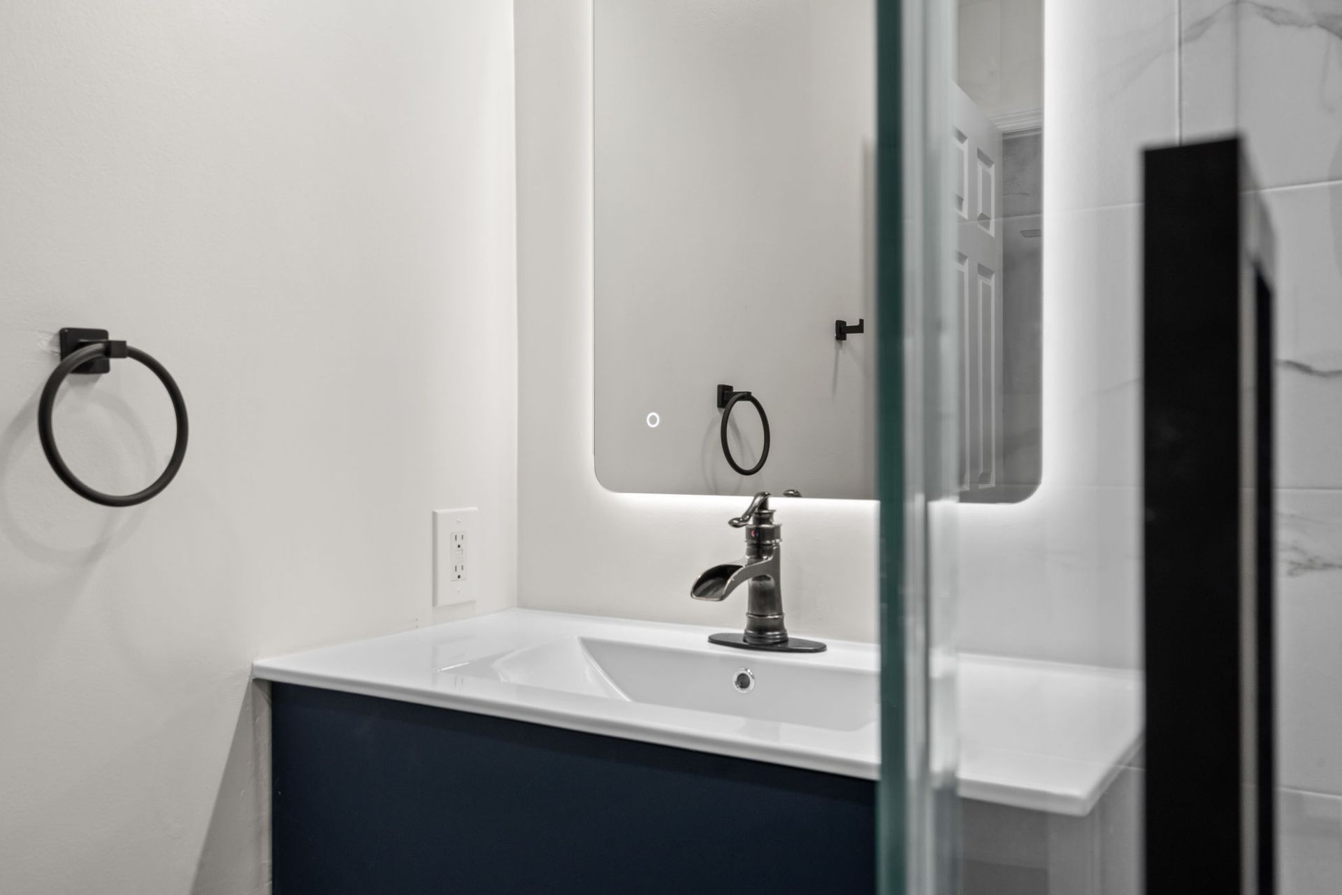 Modern bathroom vanity with mirror, chrome faucet, and towel ring beside a glass shower door