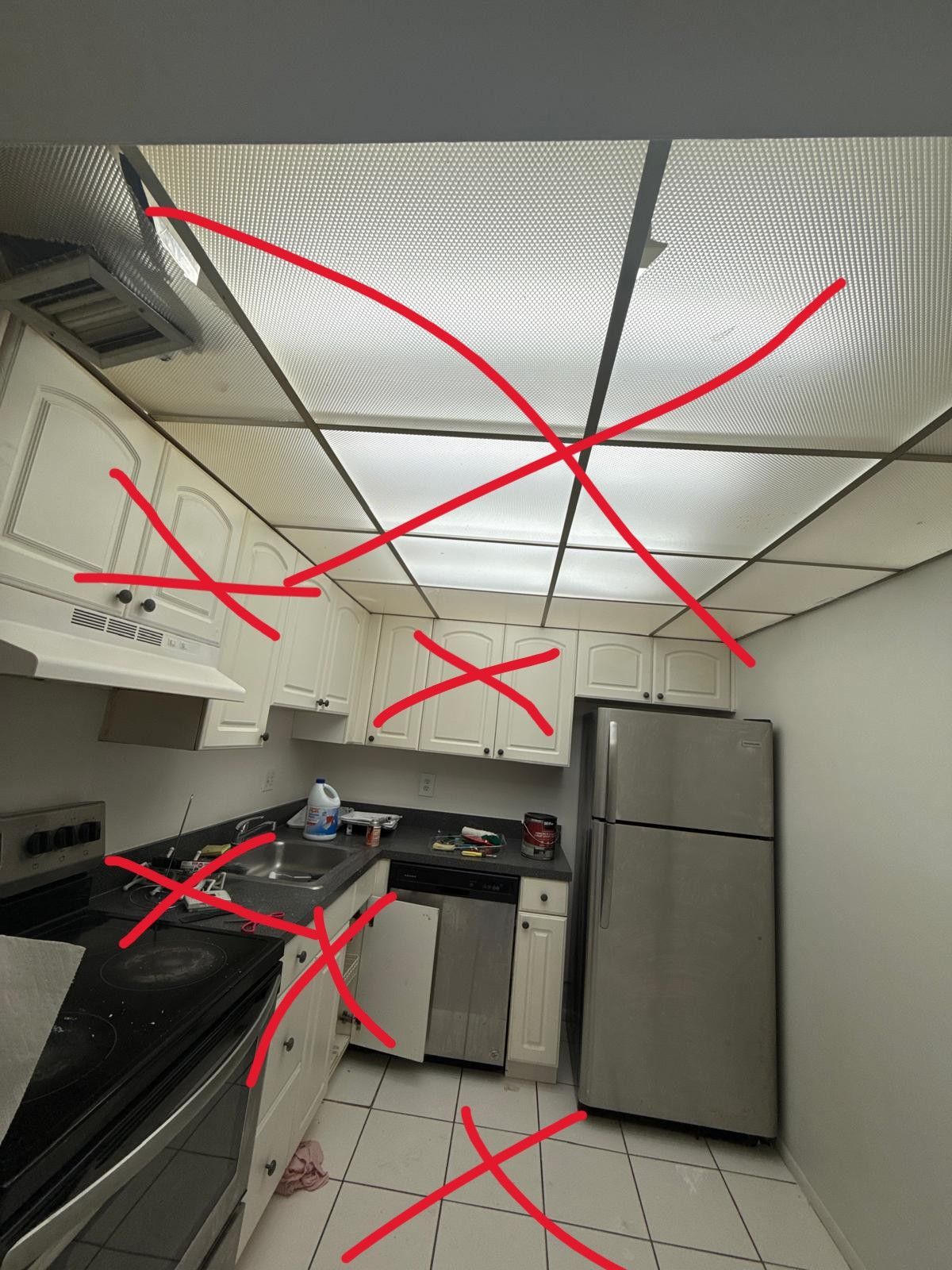 Small kitchen with stainless steel fridge, stove, cabinets, and patterned ceiling lights.