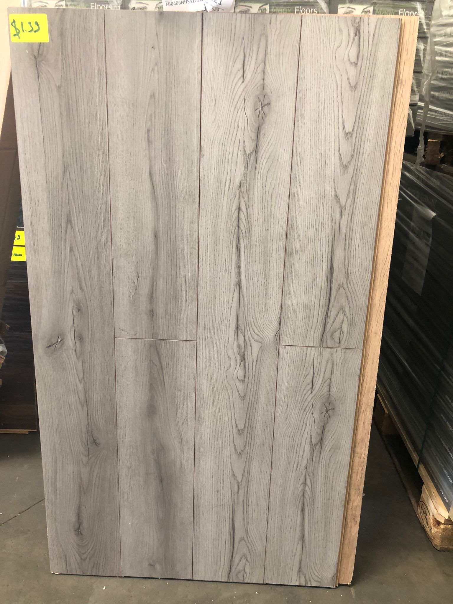 Gray wood-look tile slab displayed upright in a warehouse or showroom aisle