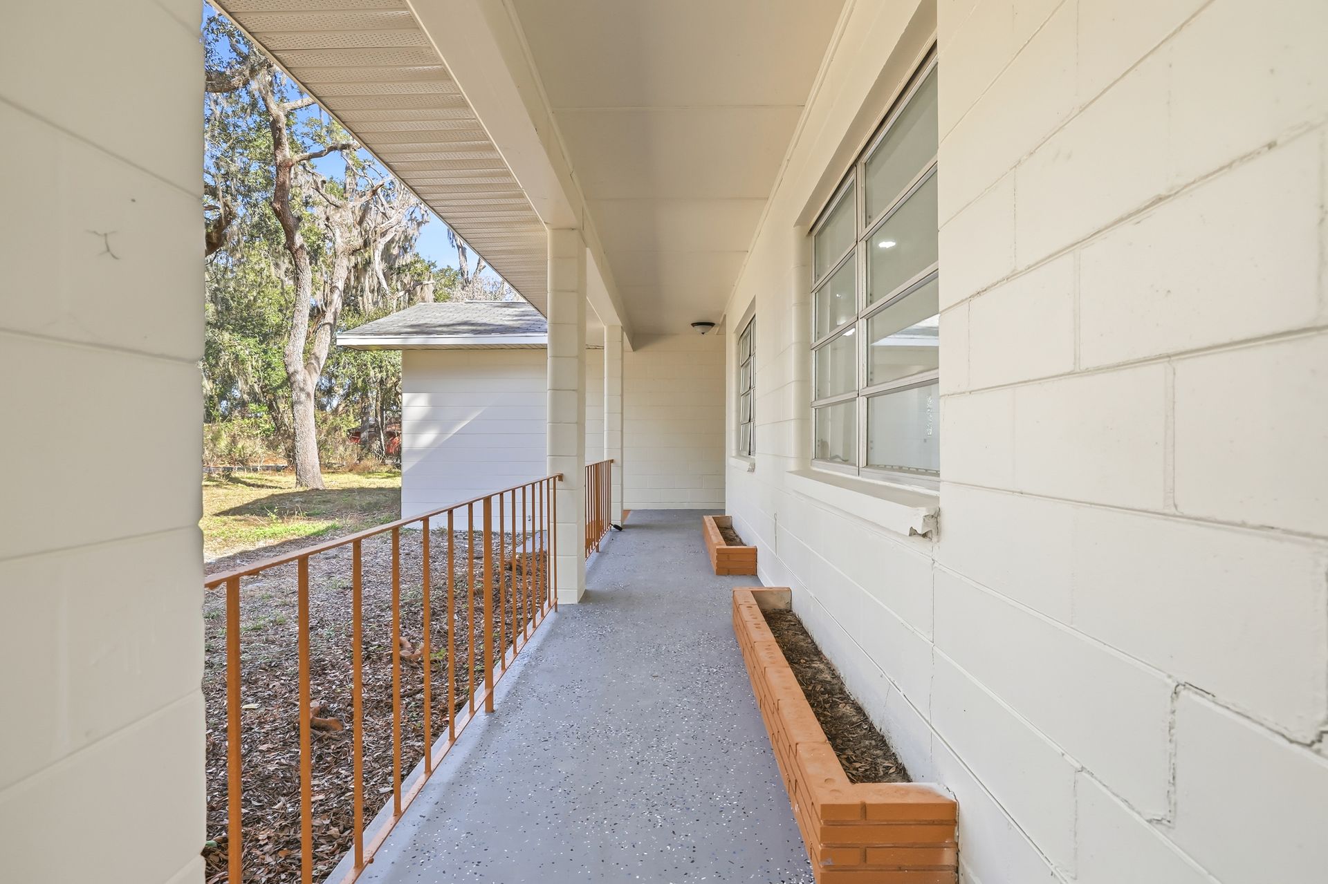 Covered apartment walkway with white walls, brick railing, and concrete floor in daylight