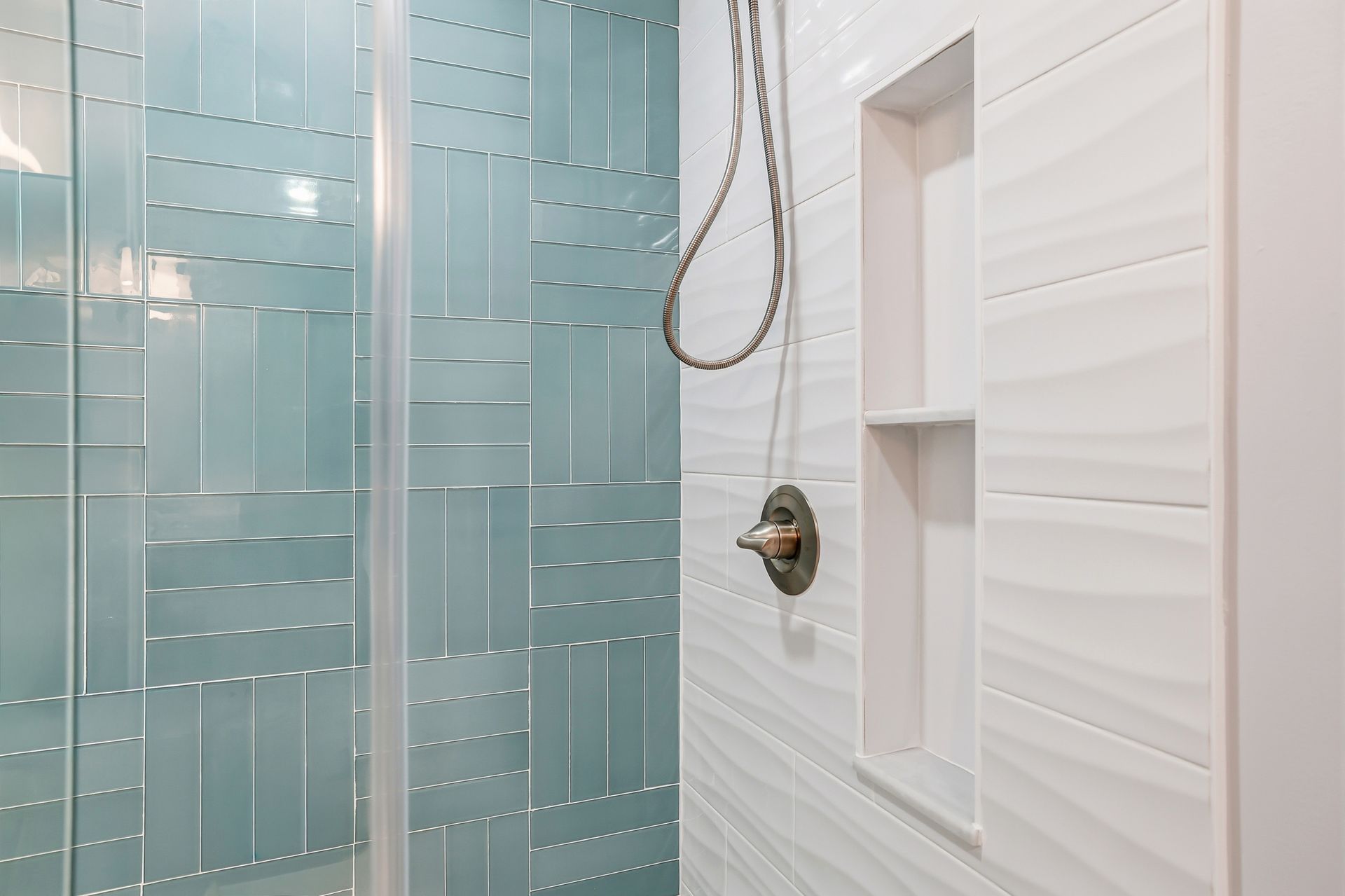 Modern shower with blue glass tiles, white walls, and a handheld showerhead.