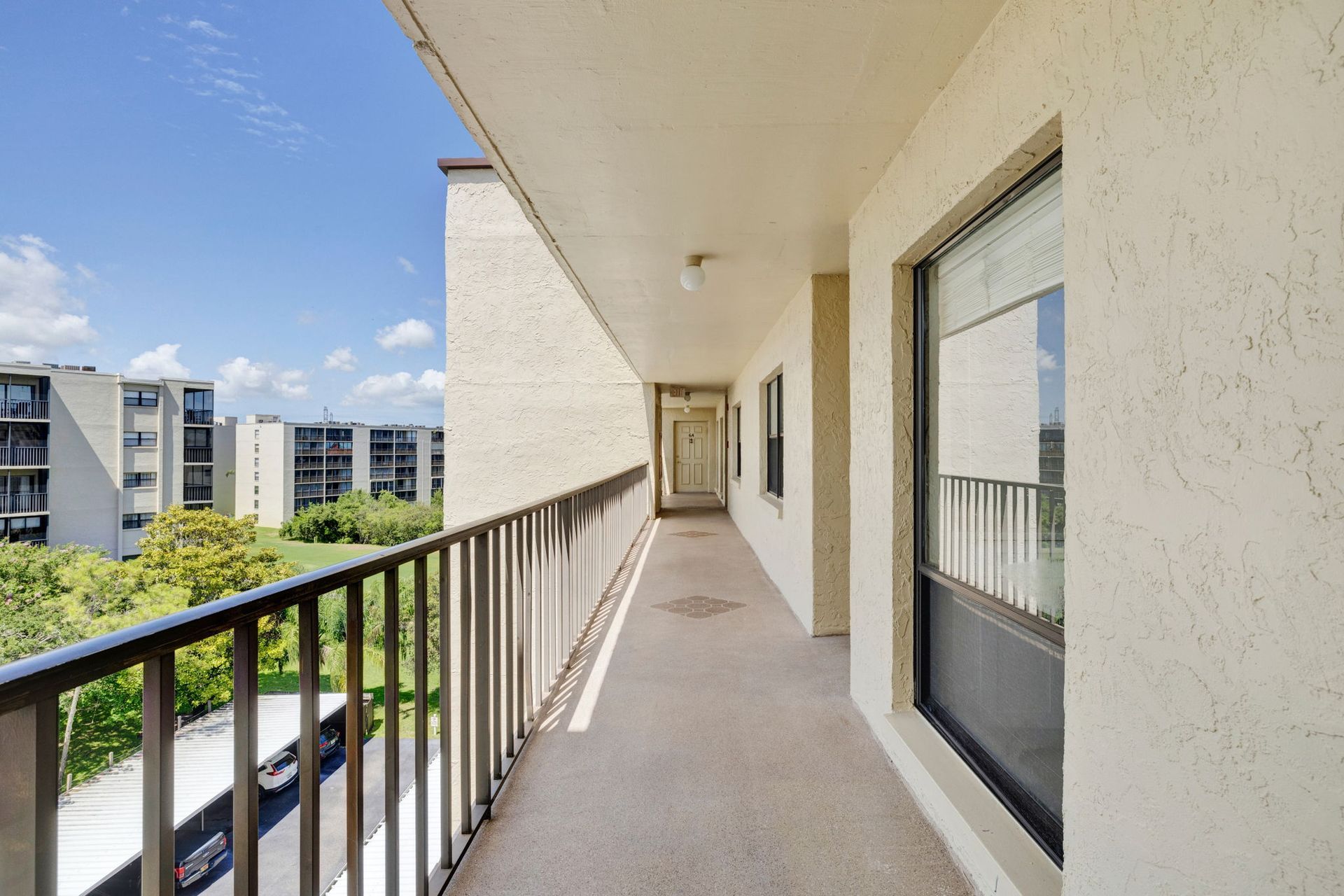 Apartment balcony walkway with metal railing, white walls, and a view of nearby buildings and trees