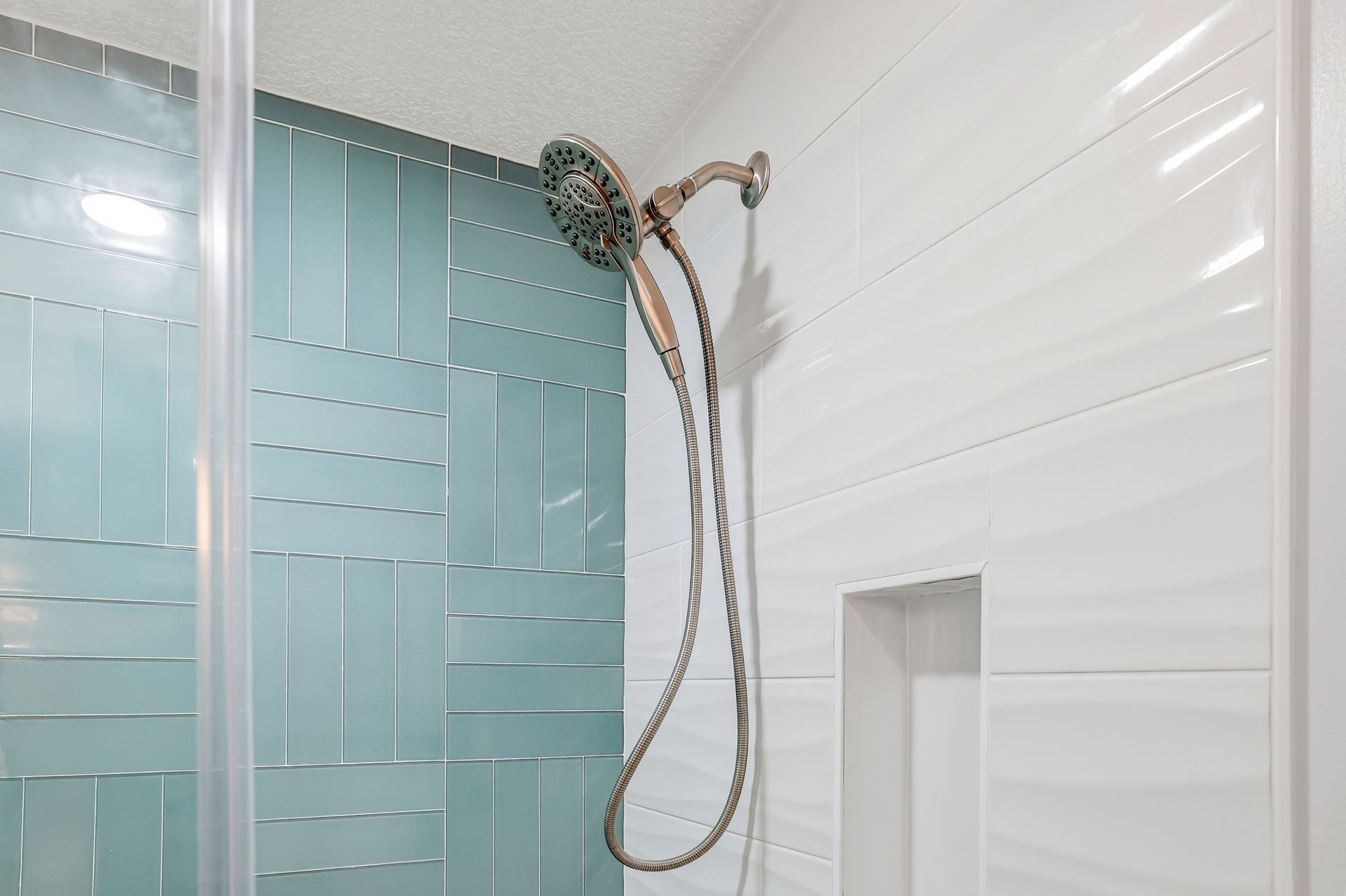 Bathroom shower with aqua tile accent wall, white tiled walls, and a handheld showerhead.