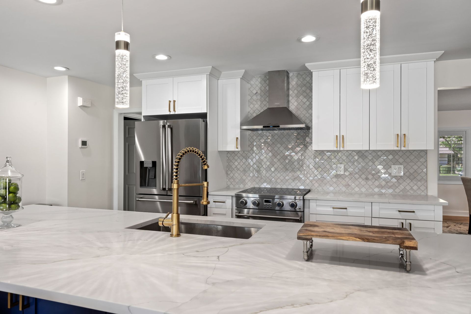 Modern white kitchen with marble island, gold faucet, stainless appliances, and pendant lights