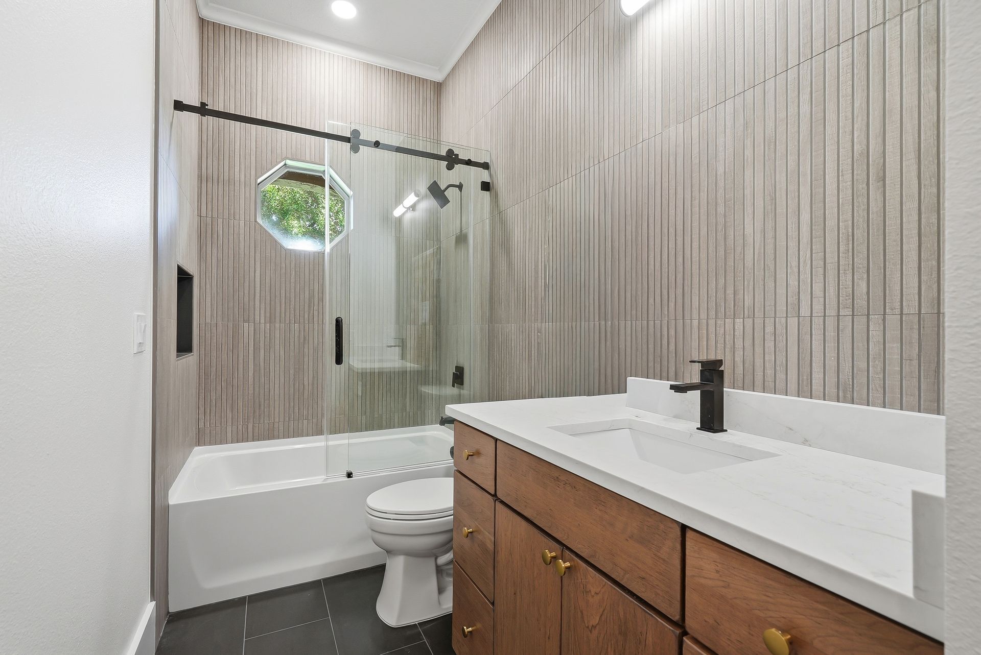 Tub-shower combo with sliding glass door, vertical wood-look tile, and wood vanity with brass hardware
