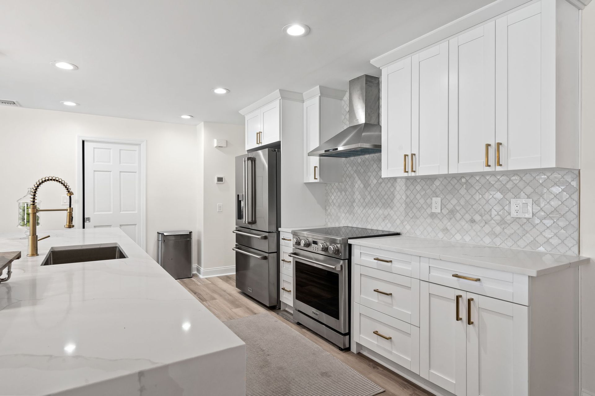 Bright white modern kitchen with island, stainless steel appliances, and gold-accent cabinet handles