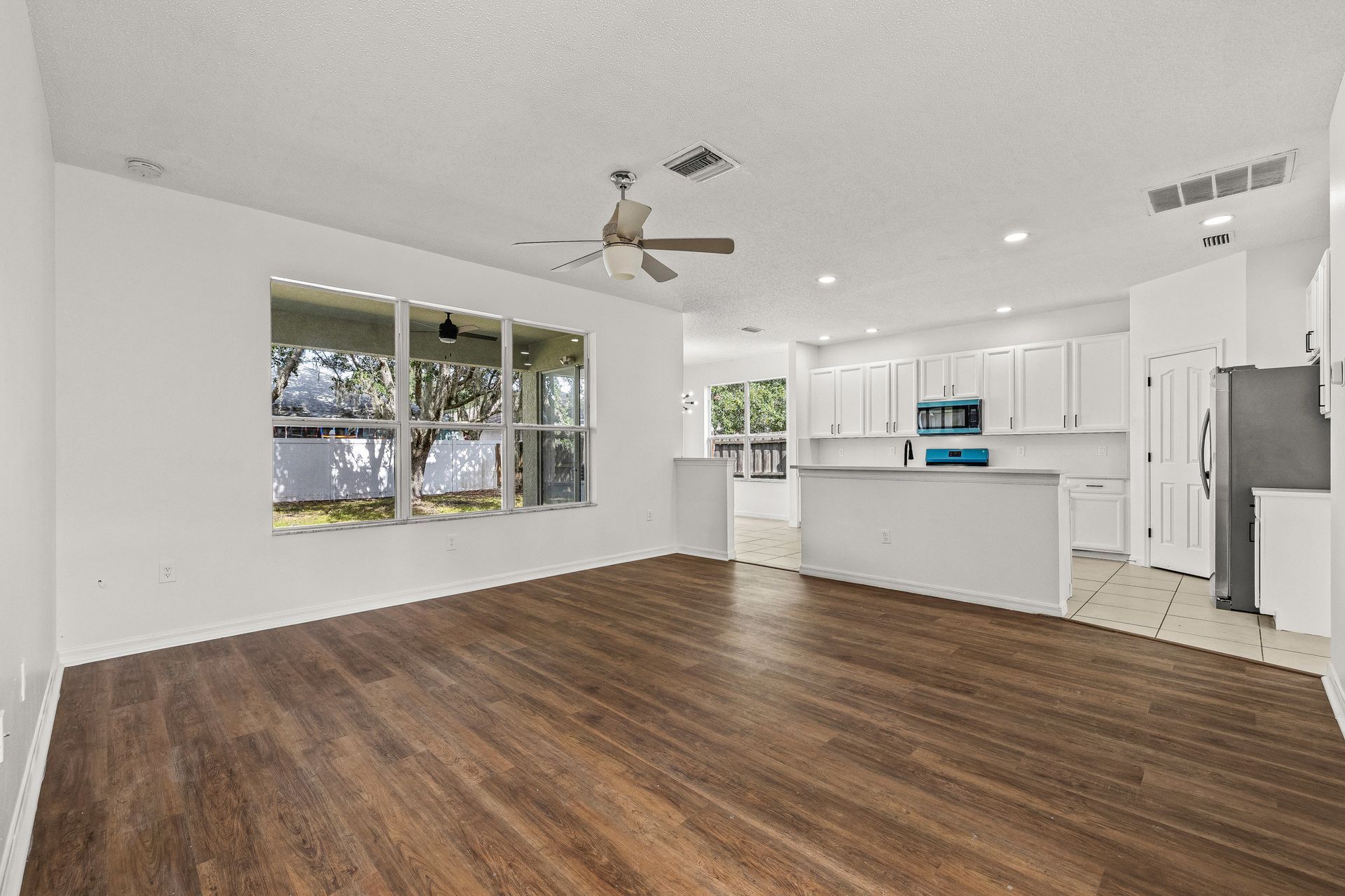 Empty open-plan living room and white kitchen with dark wood floors and large windows