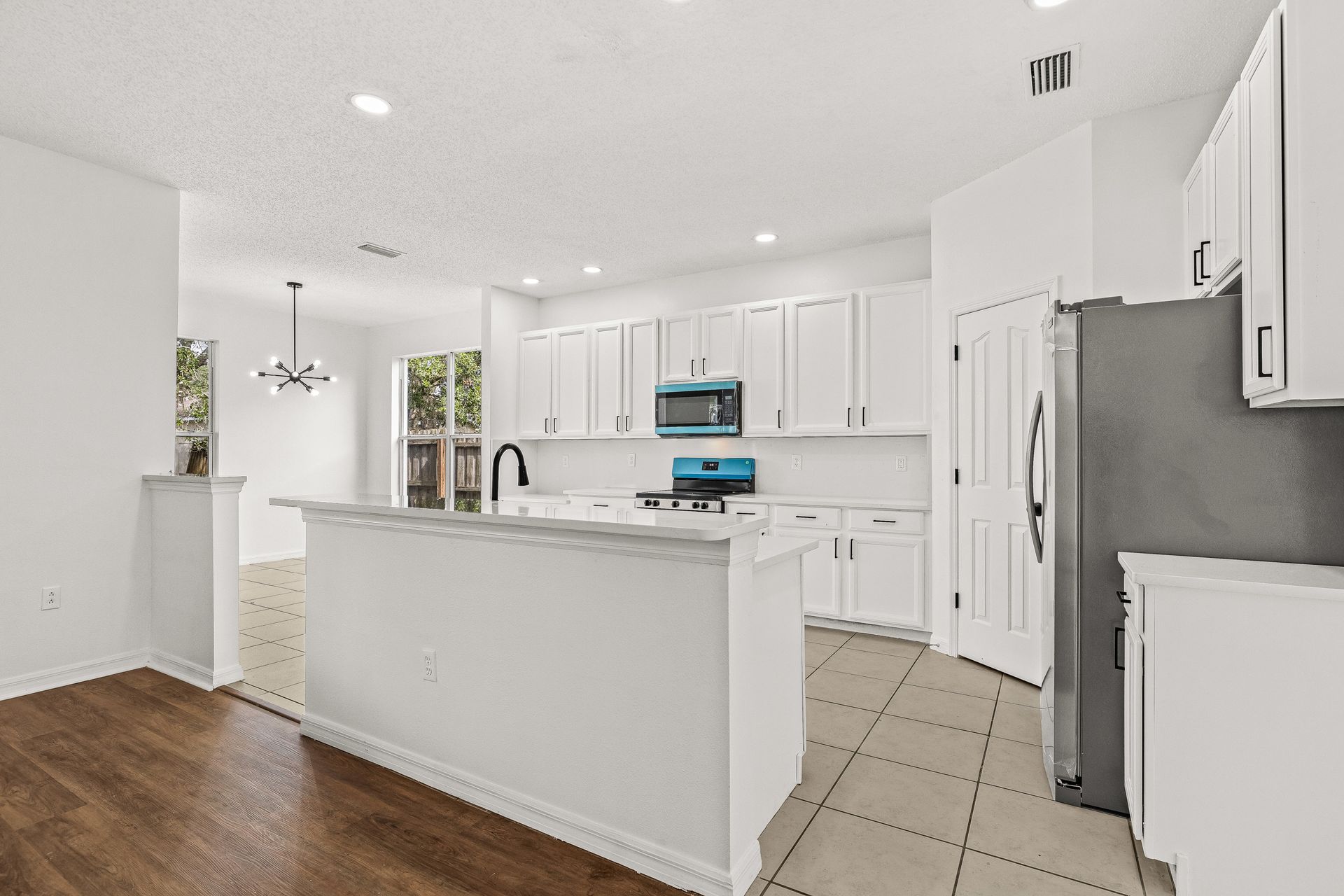 Bright white kitchen with island, stainless appliances, tiled floor, and wood flooring area