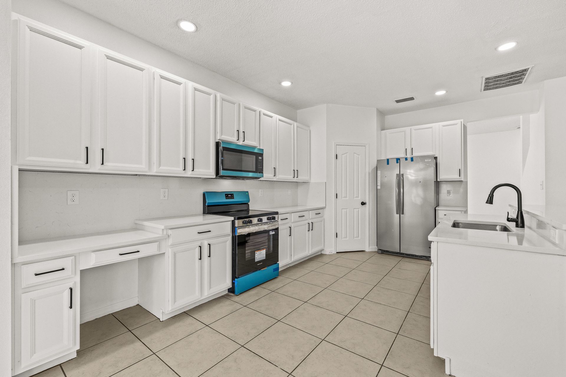 Bright white modern kitchen with stainless steel appliances, tile floor, and large island sink