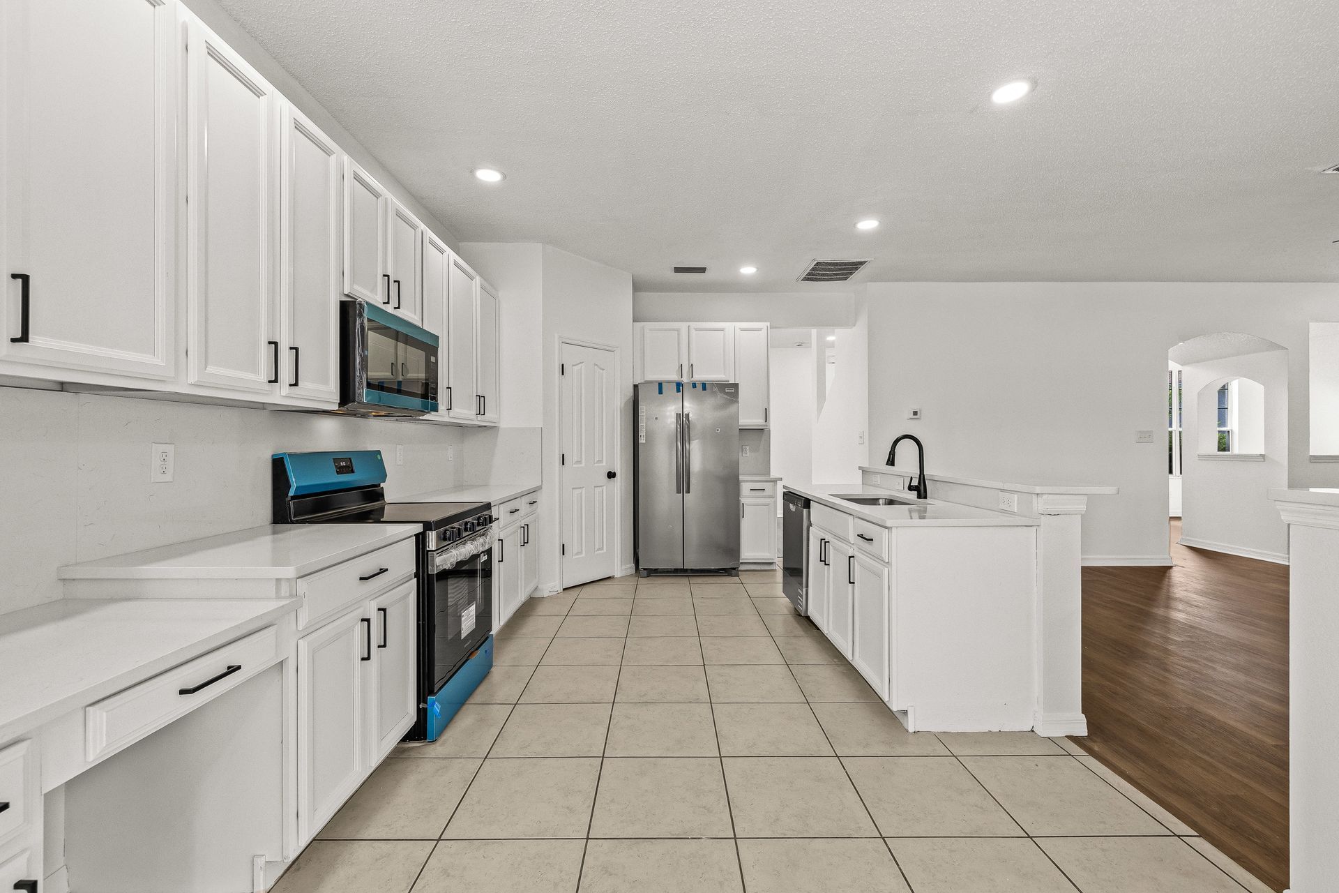 Bright white modern kitchen with stainless steel appliances, tile floor, and a central island