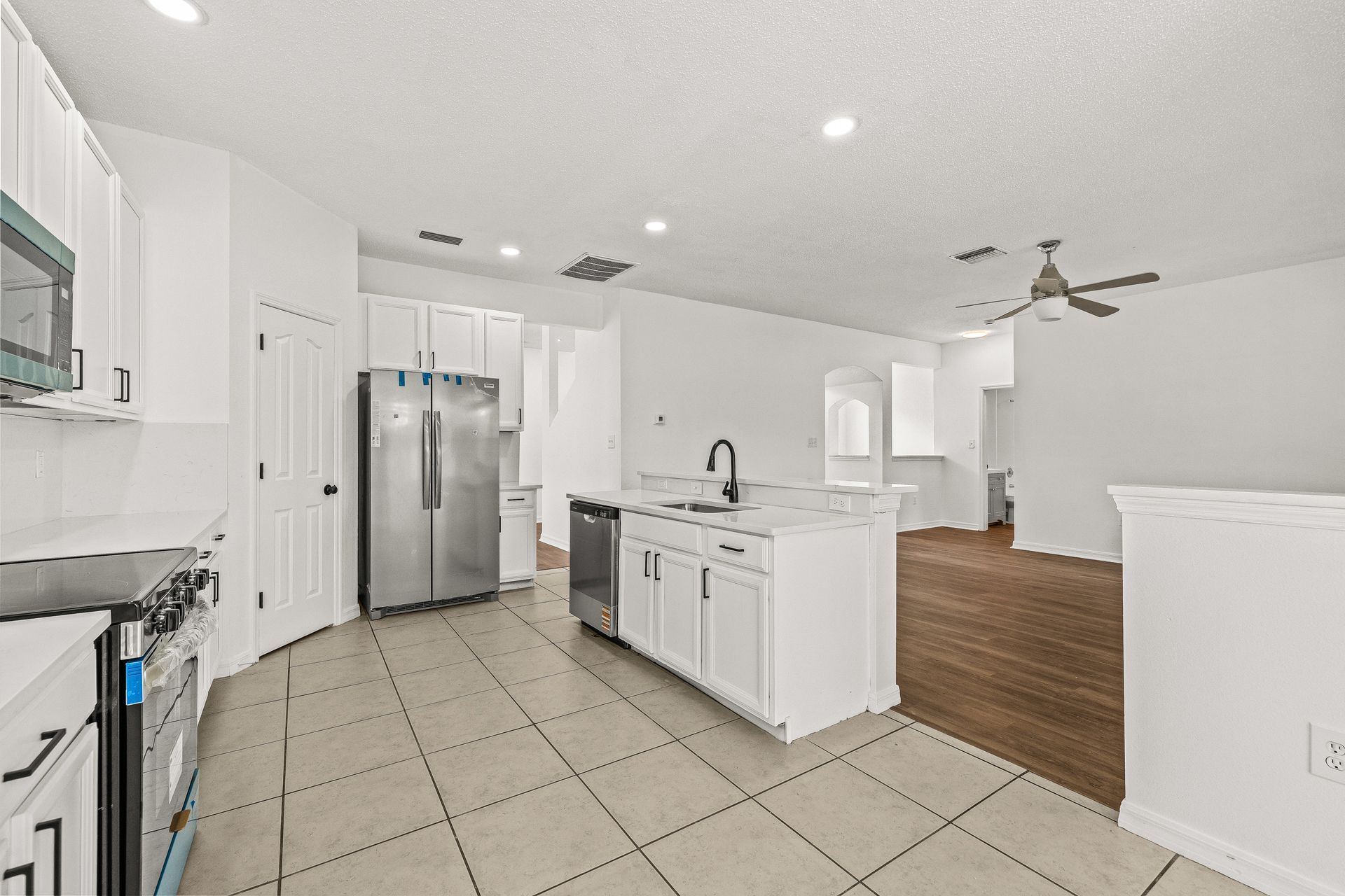 Bright white kitchen with stainless steel fridge, island, tile floor, and hardwood dining area.