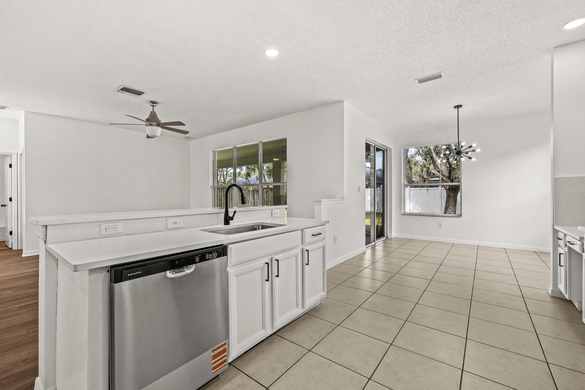 Bright white kitchen and dining area with tile floor, island sink, and stainless dishwasher near sliding glass doors