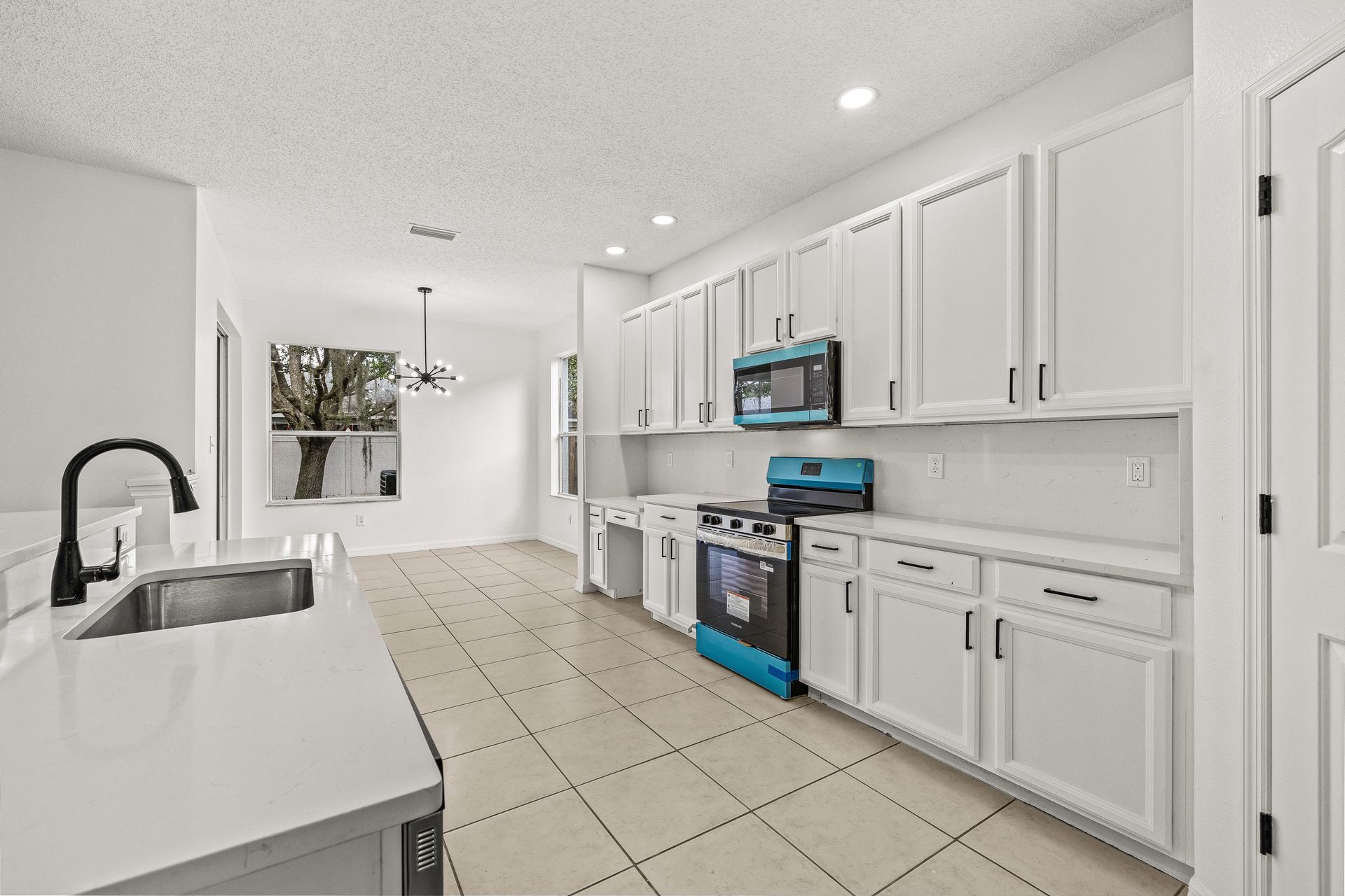 Bright white modern kitchen with tile floor, cabinets, stainless appliances, and island sink