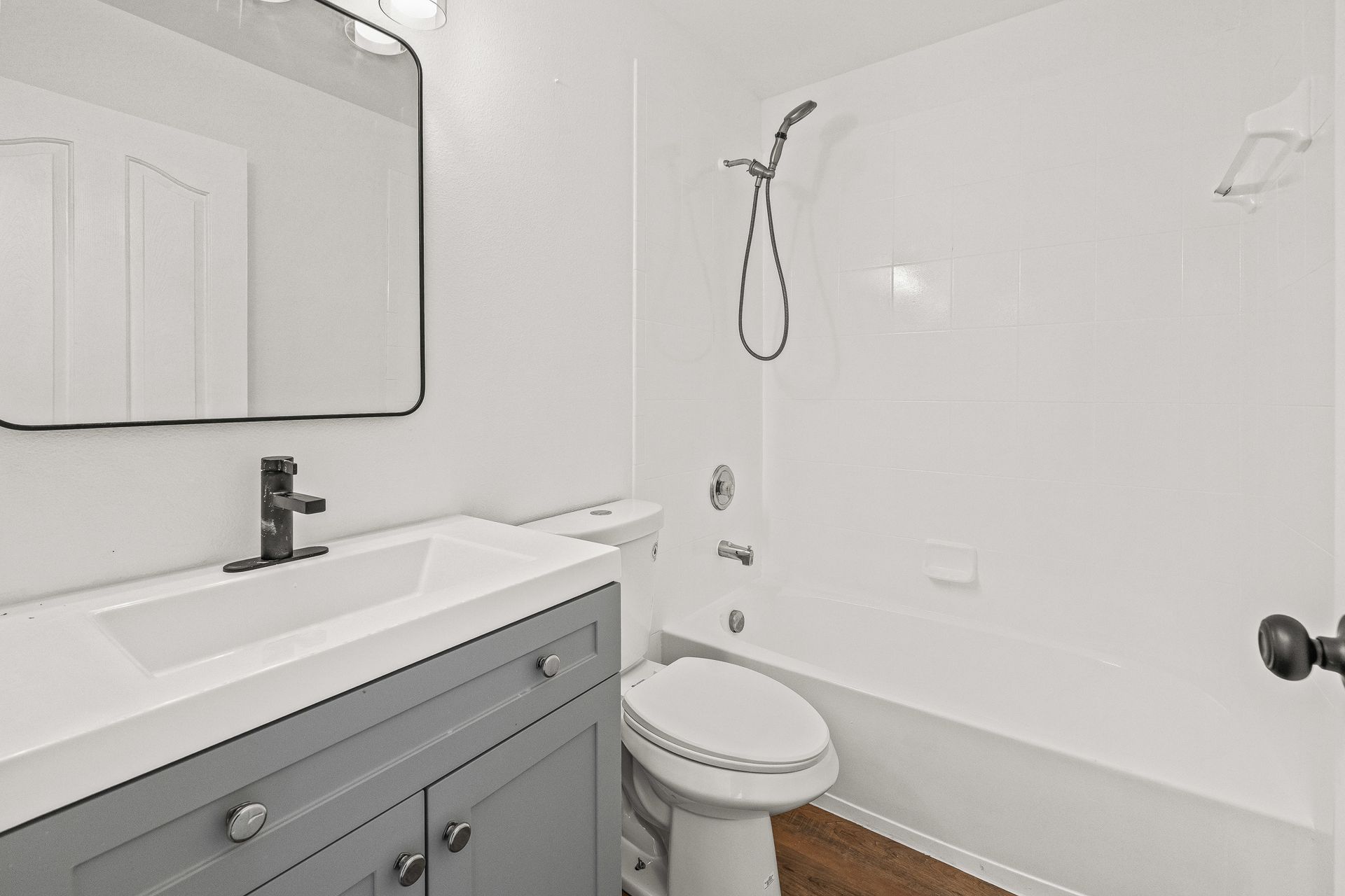 Small white bathroom with a sink, mirror, toilet, shower, and gray vanity.