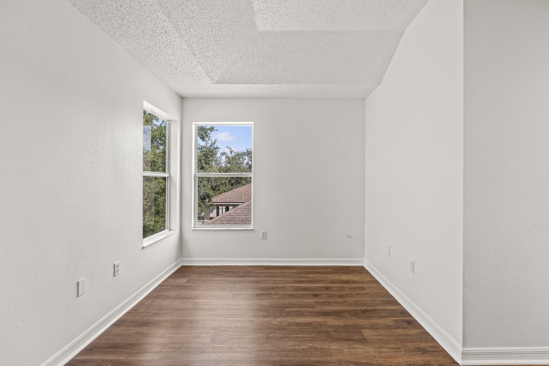 Empty white room with wood floors and two windows letting in daylight