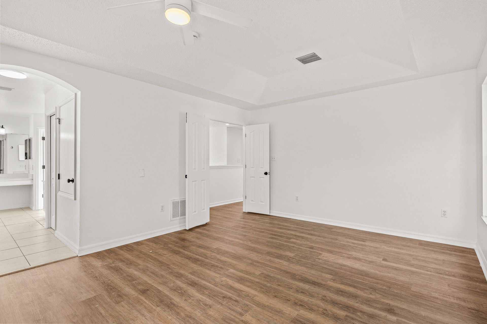 Empty white room with wood flooring and an open doorway to a hallway