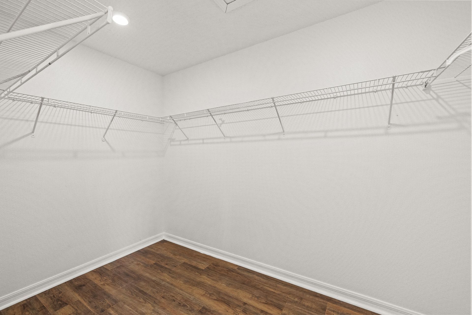Empty white walk-in closet with wire shelving and wood floor