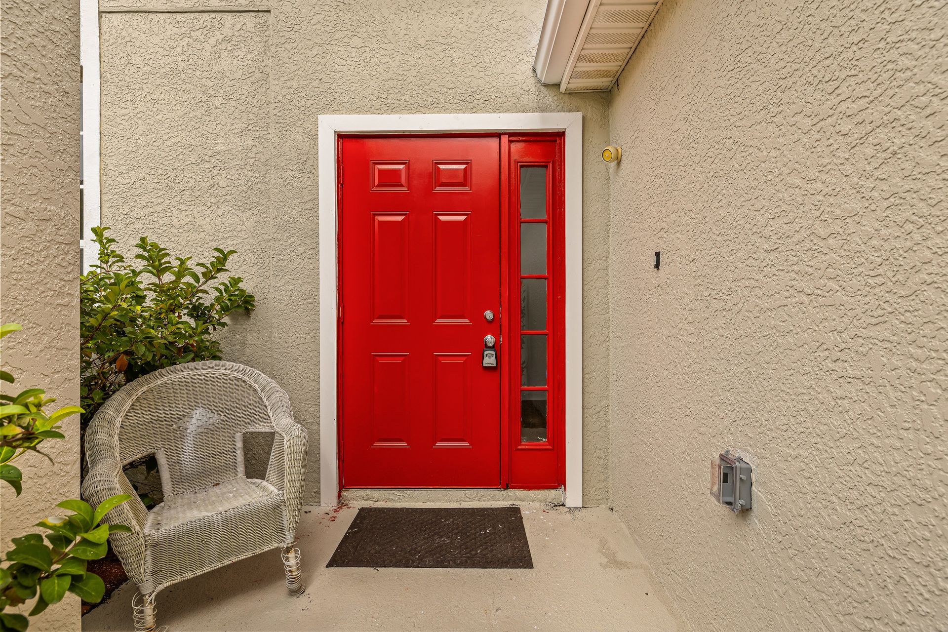 Bright red front door beside a wicker chair on a beige stucco porch